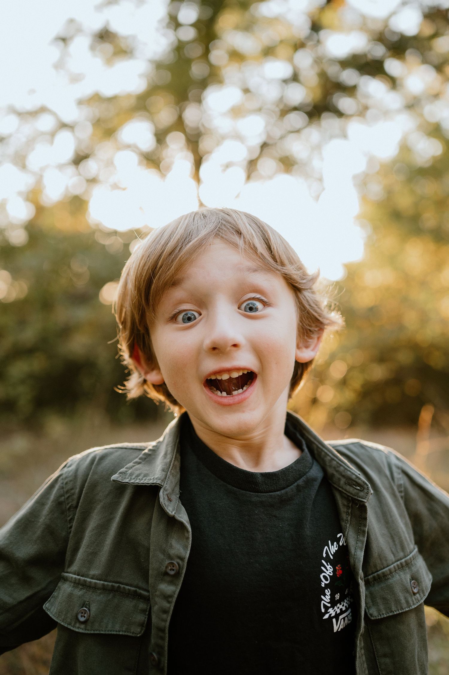 An excited expression captured in golden sunlight while wearing an olive green jacket outdoors.