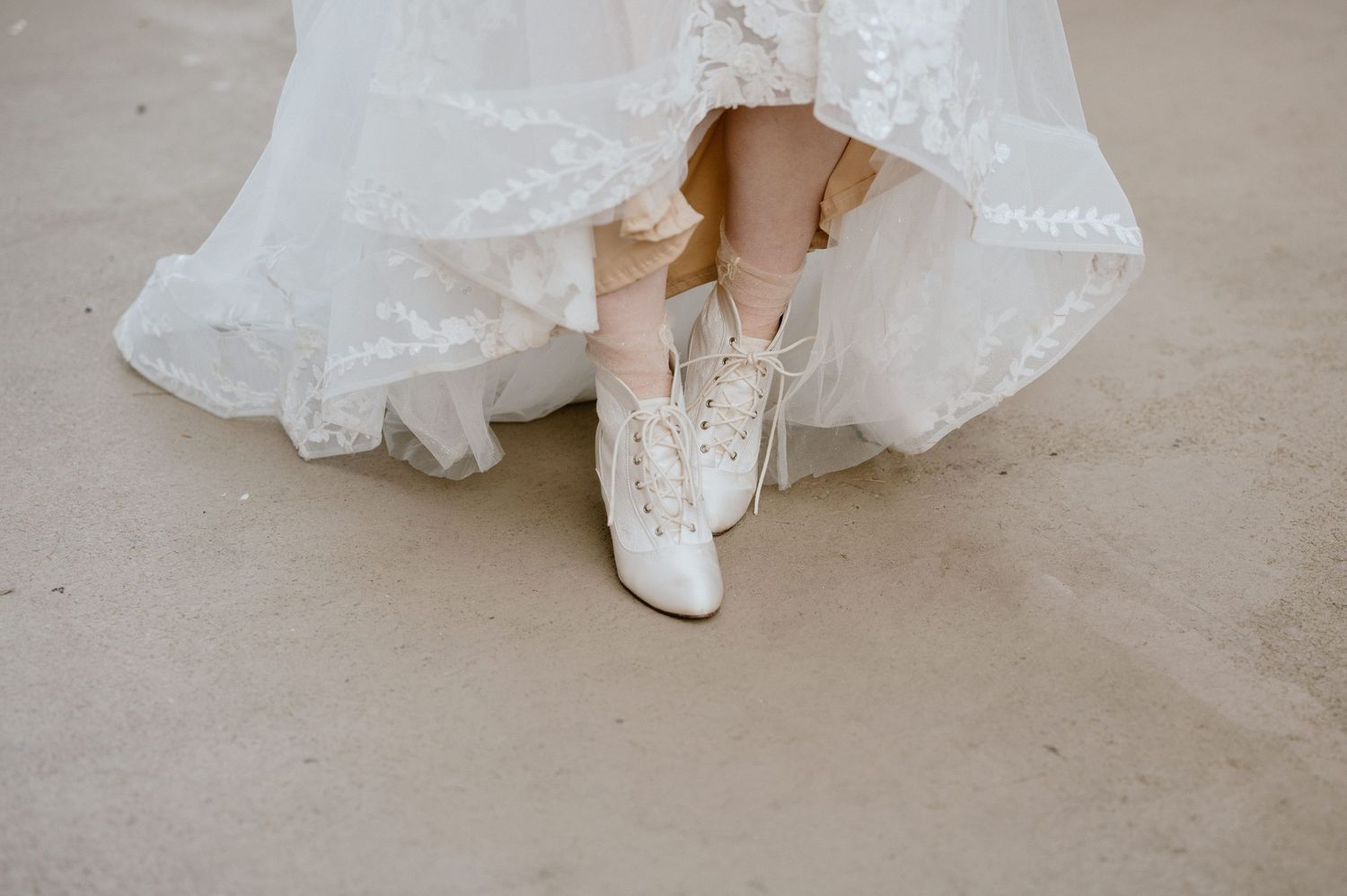 Wedding dress hem reveals elegant white lace bridal sneakers.
