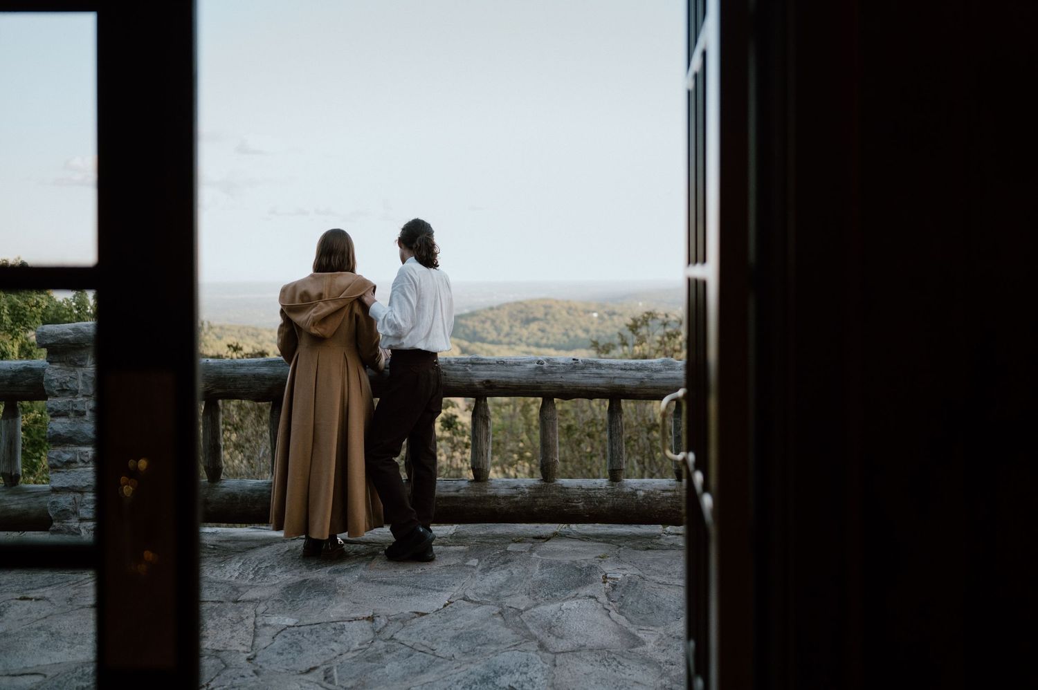 Two figures standing on a stone balcony overlooking a scenic landscape.