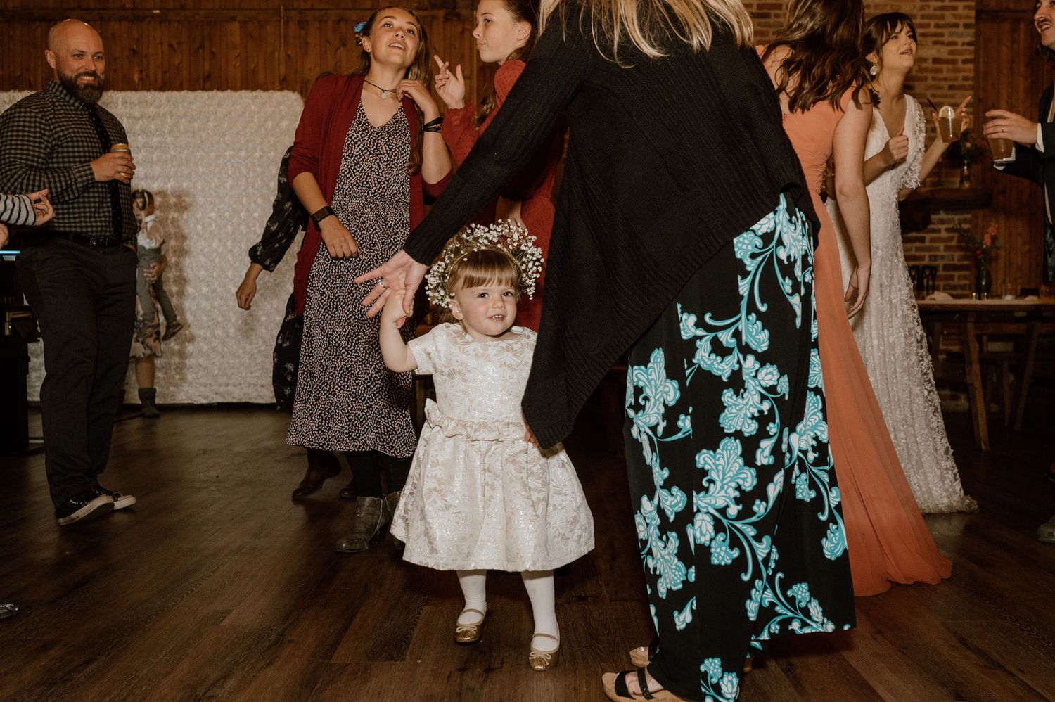 Young girl in white dress dancing at a rustic wedding reception.