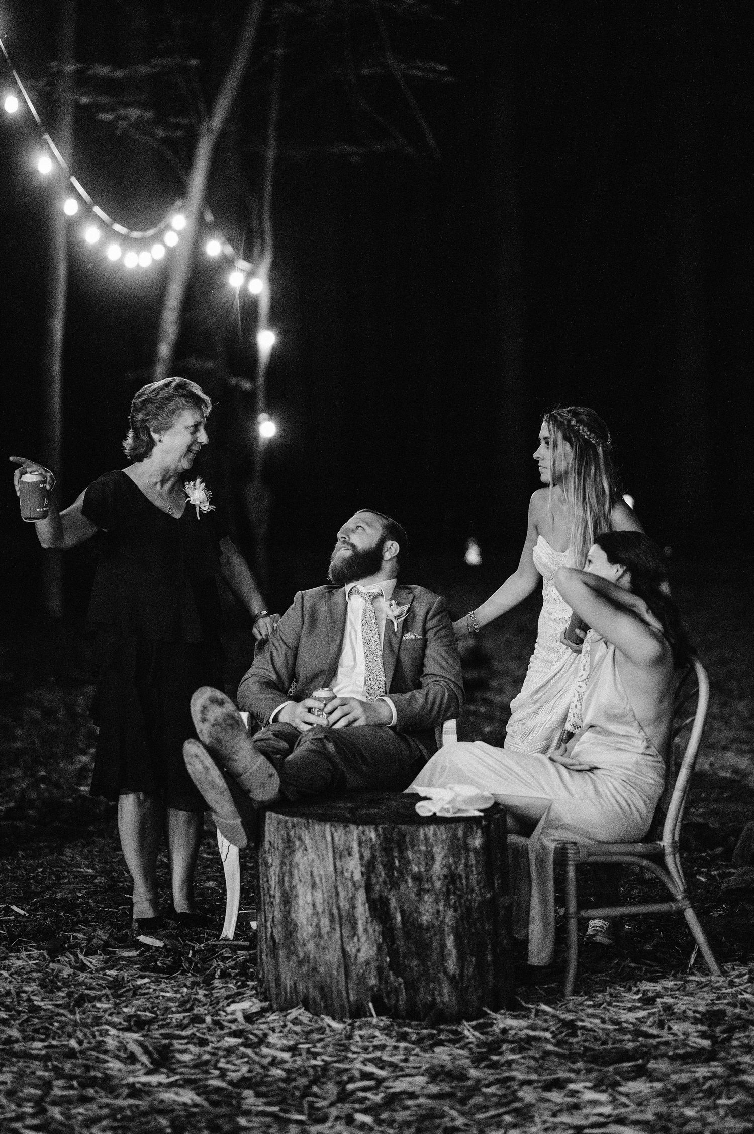 A nighttime gathering illuminated by string lights in a forest setting.