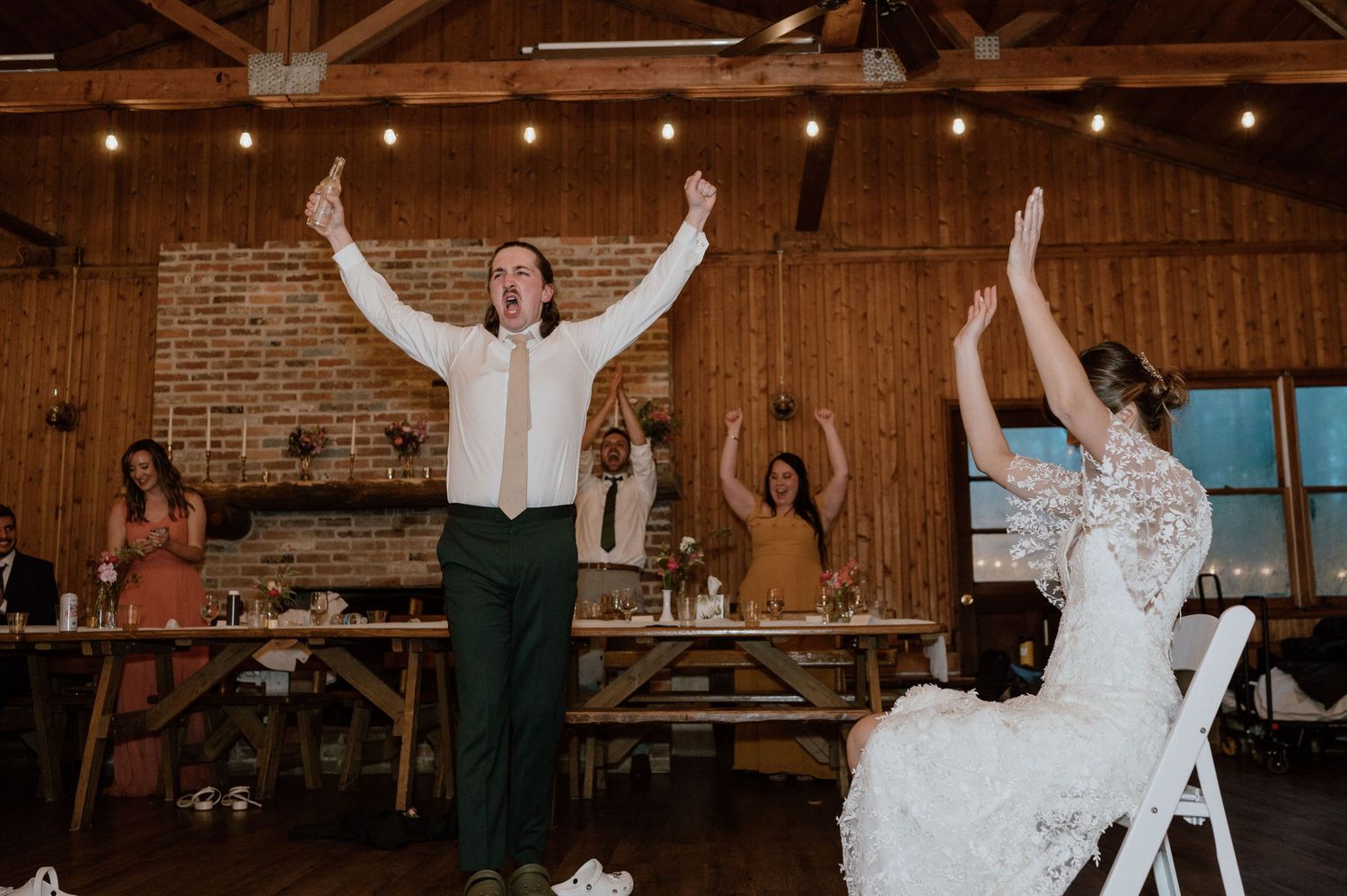 Couple celebrating with raised arms during wedding reception in rustic barn venue.