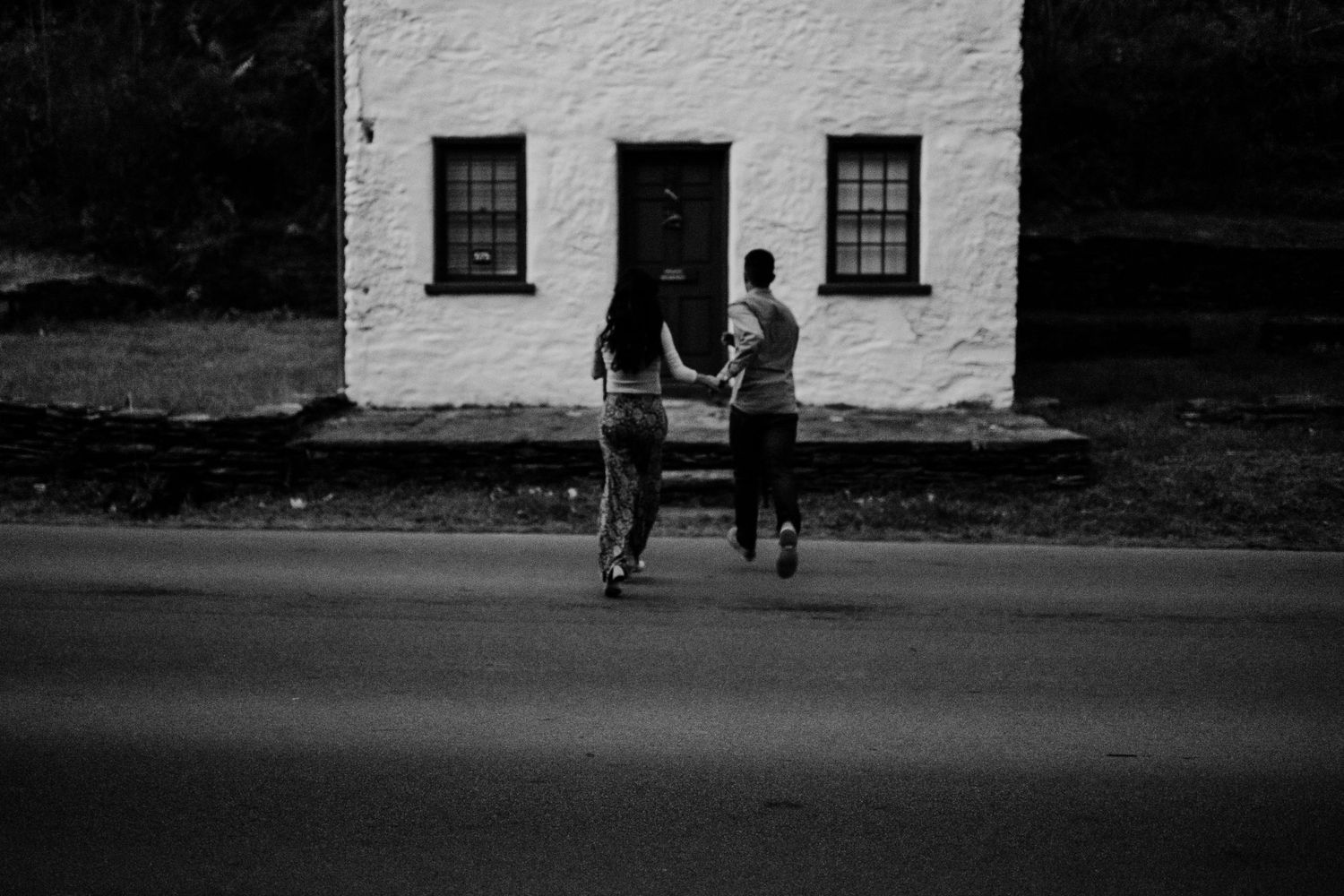A couple stands in front of a classic white building in black and white photography.