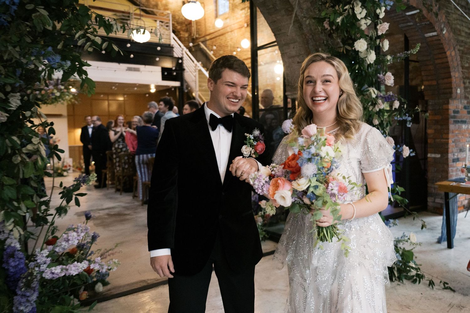 A wedding celebration in an indoor venue with floral decorations and elegant formal attire.