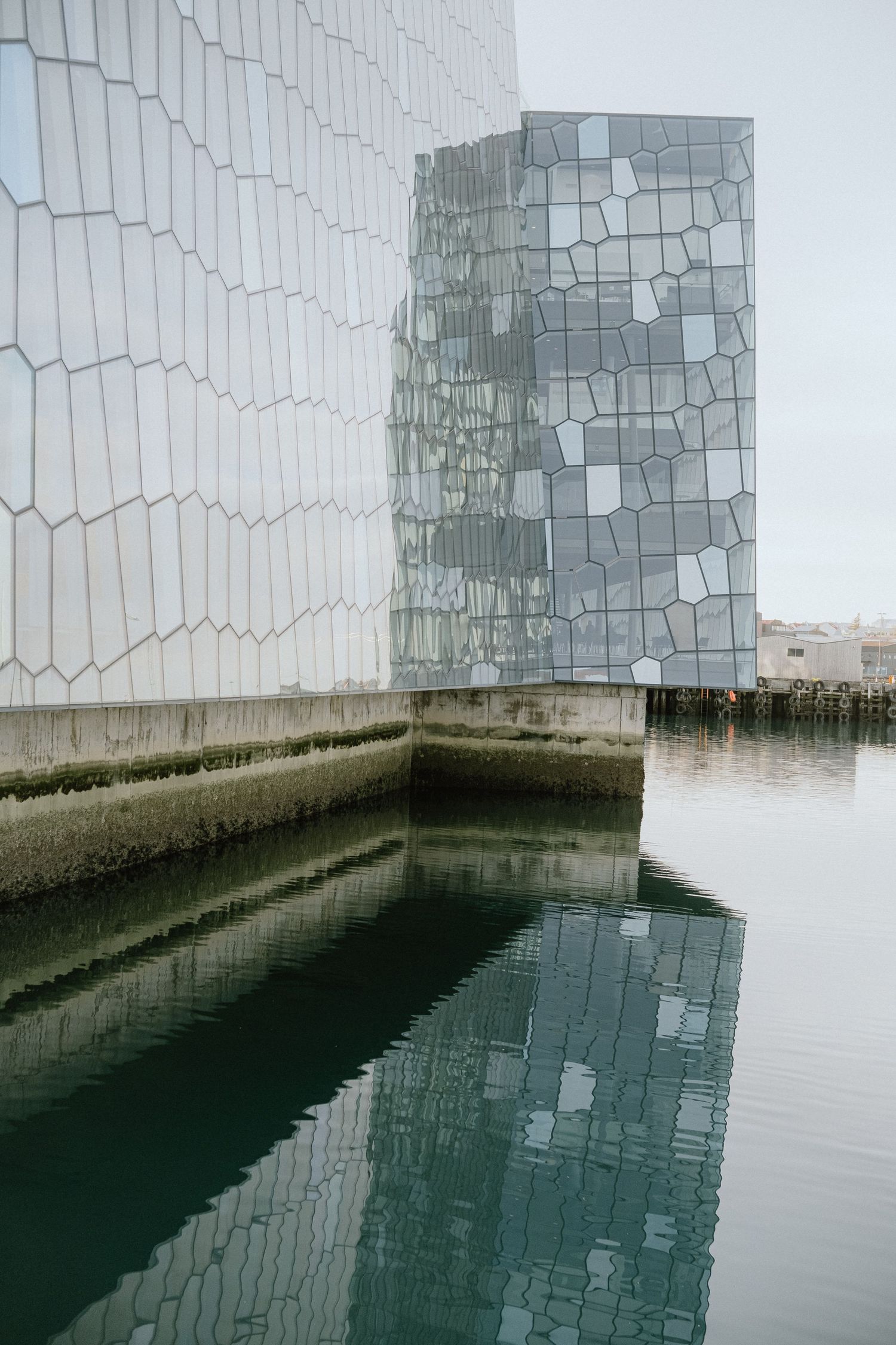 Modern glass building with geometric patterns reflects in dark water below.