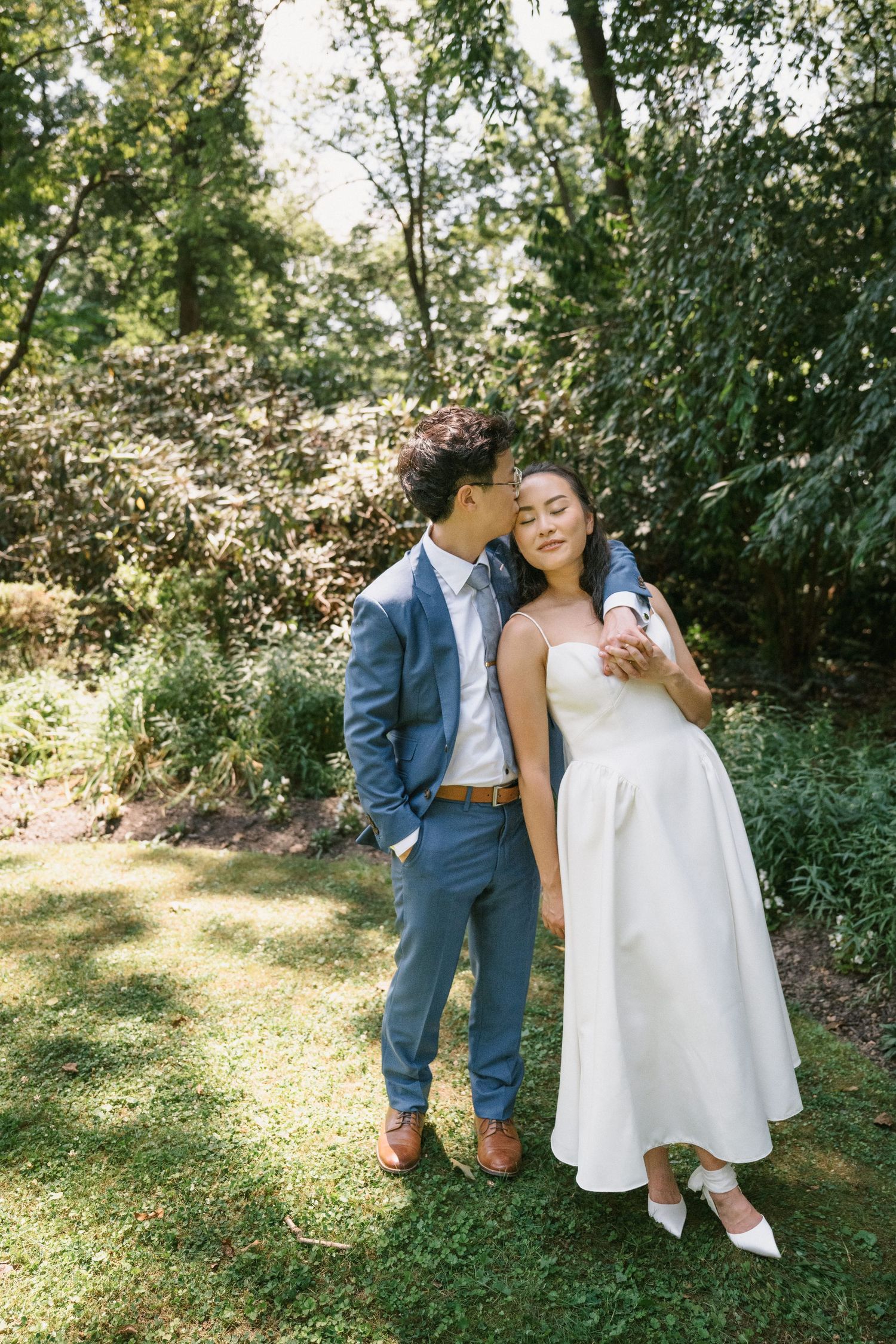 A romantic outdoor wedding moment with a couple embracing in a sunlit garden setting with lush greenery in the background.