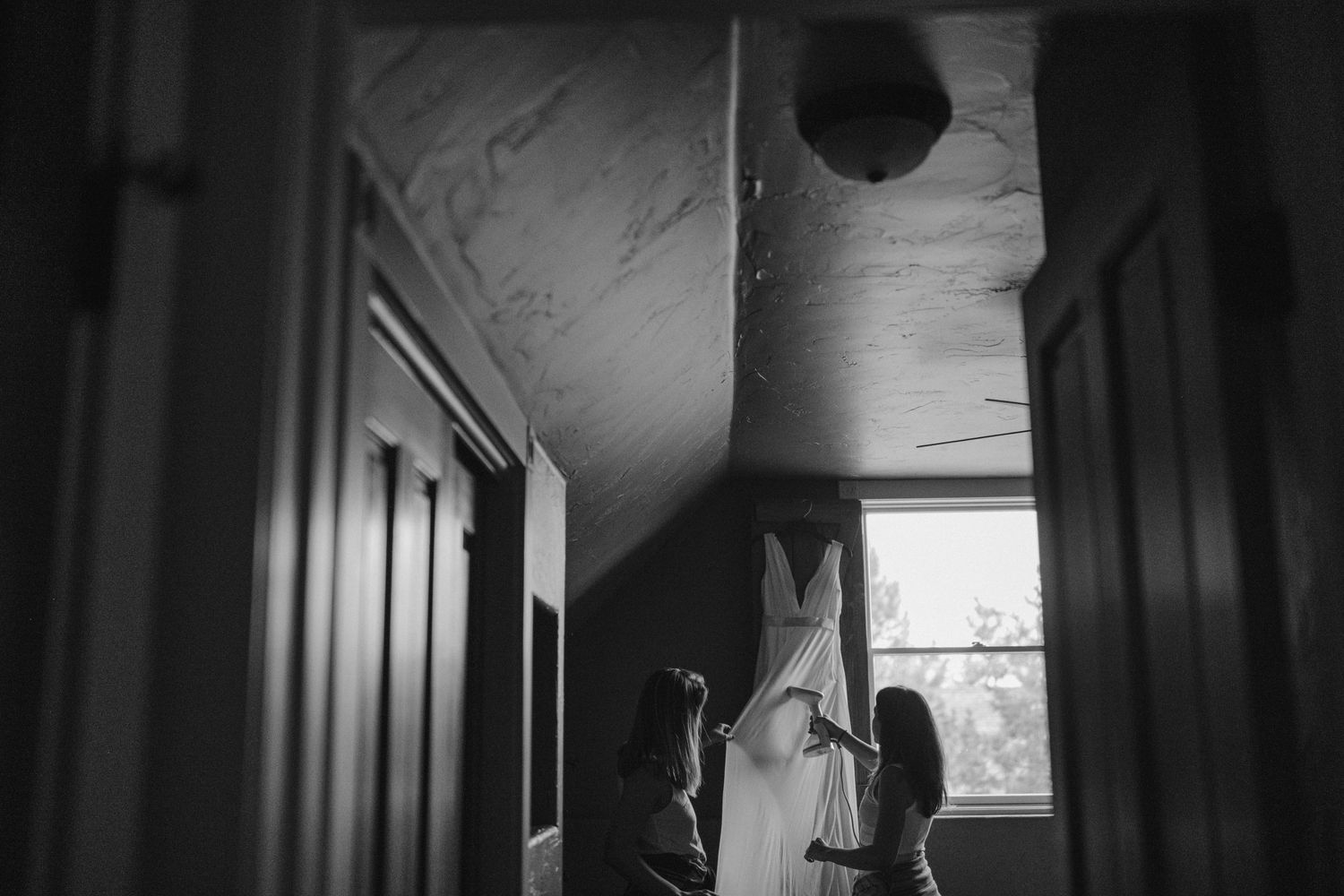 Black and white image of wedding dress being prepared in hallway.