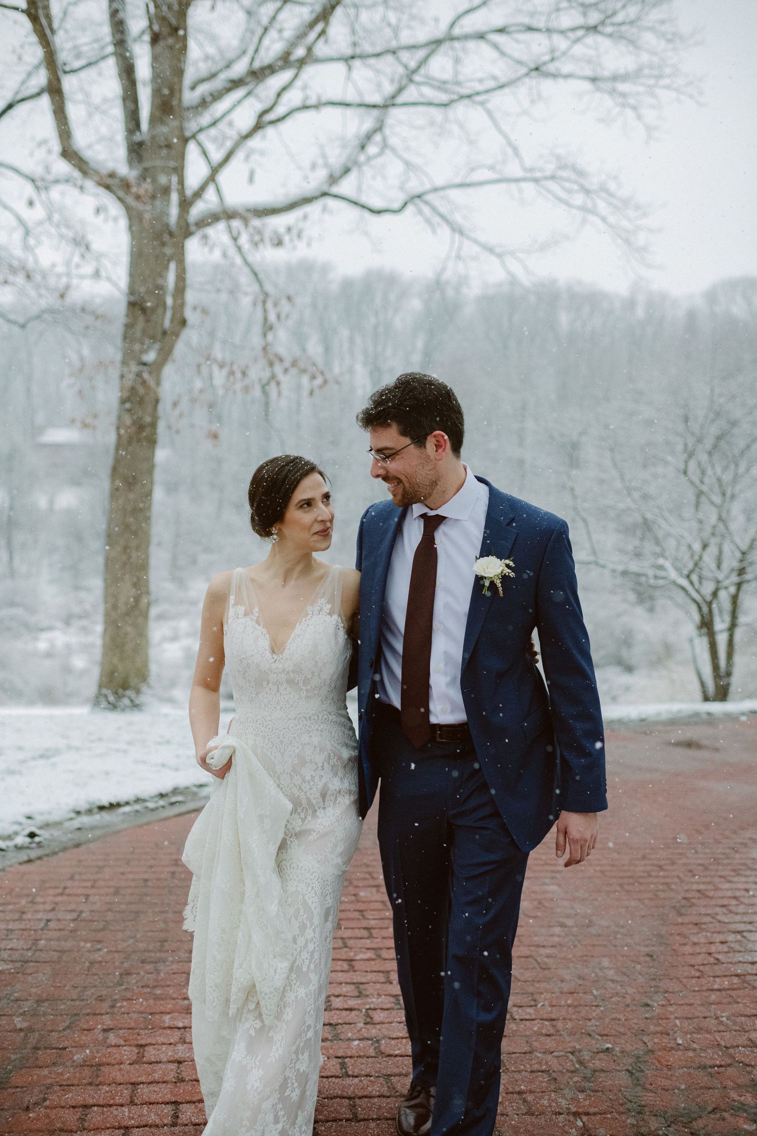 A couple strolls along a red brick path during their snowy winter wedding.