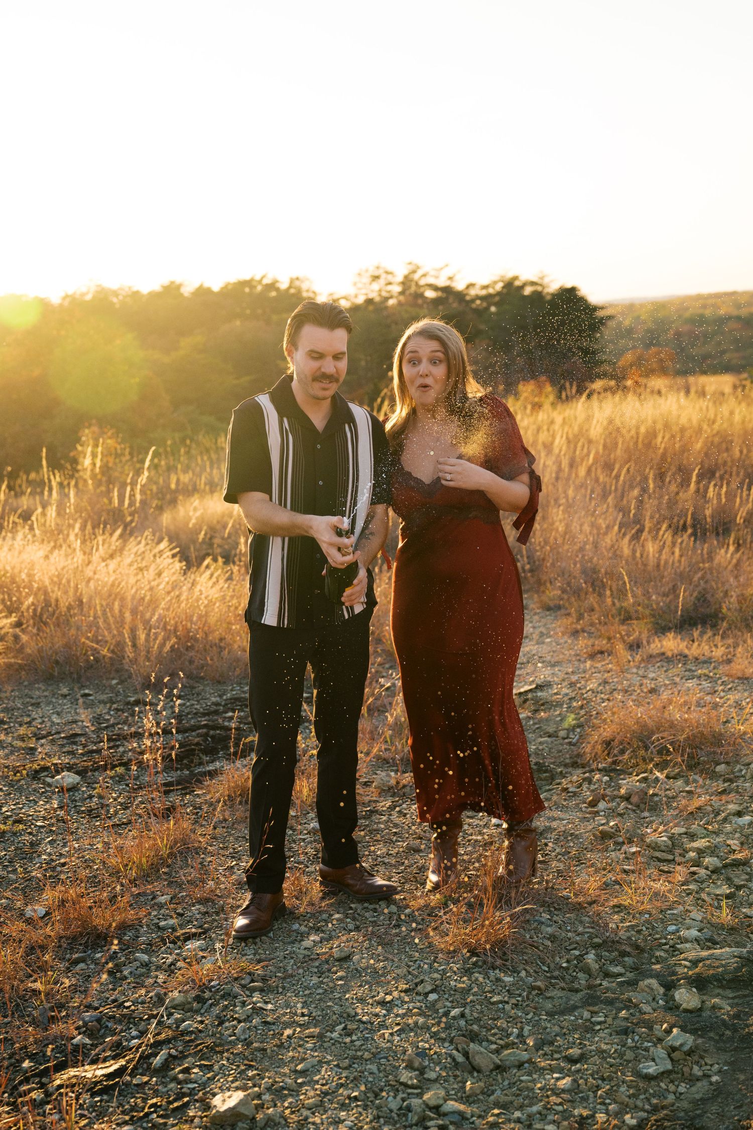 A couple poses together in a sun-drenched field during golden hour with warm natural lighting.