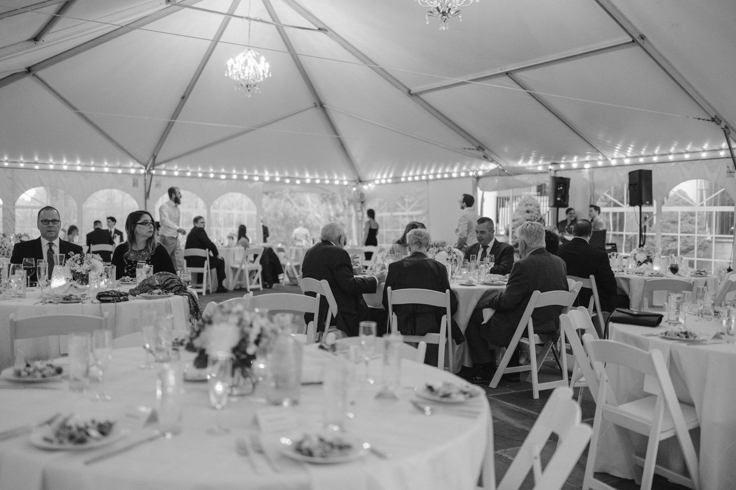 Wedding reception under a white tent with string lights and round tables.