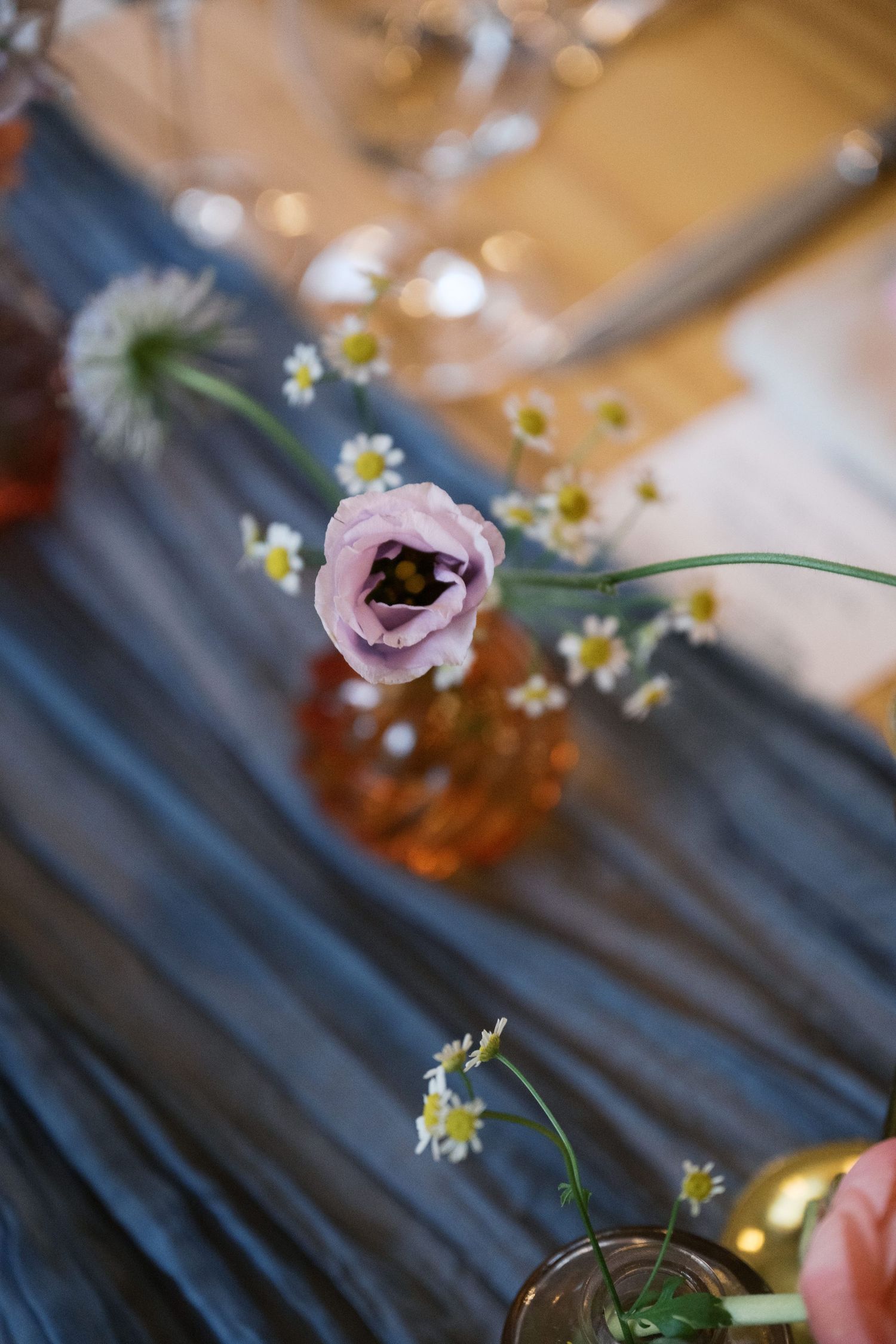 Close-up of pink ranunculus and daisies in small vases with blue fabric runner.