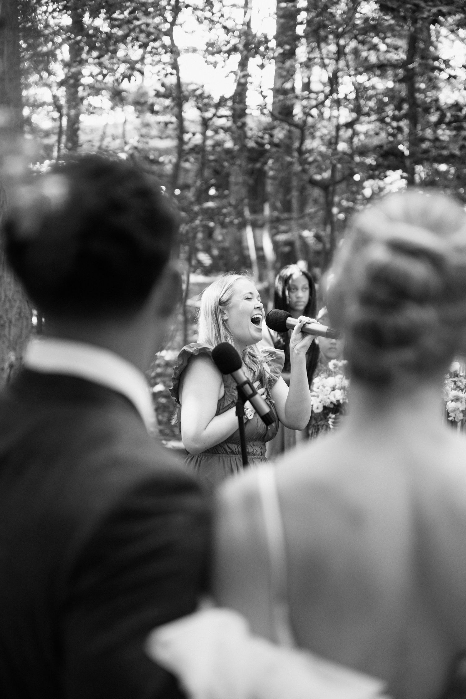 A singer passionately performs during an outdoor wedding ceremony in a wooded setting.