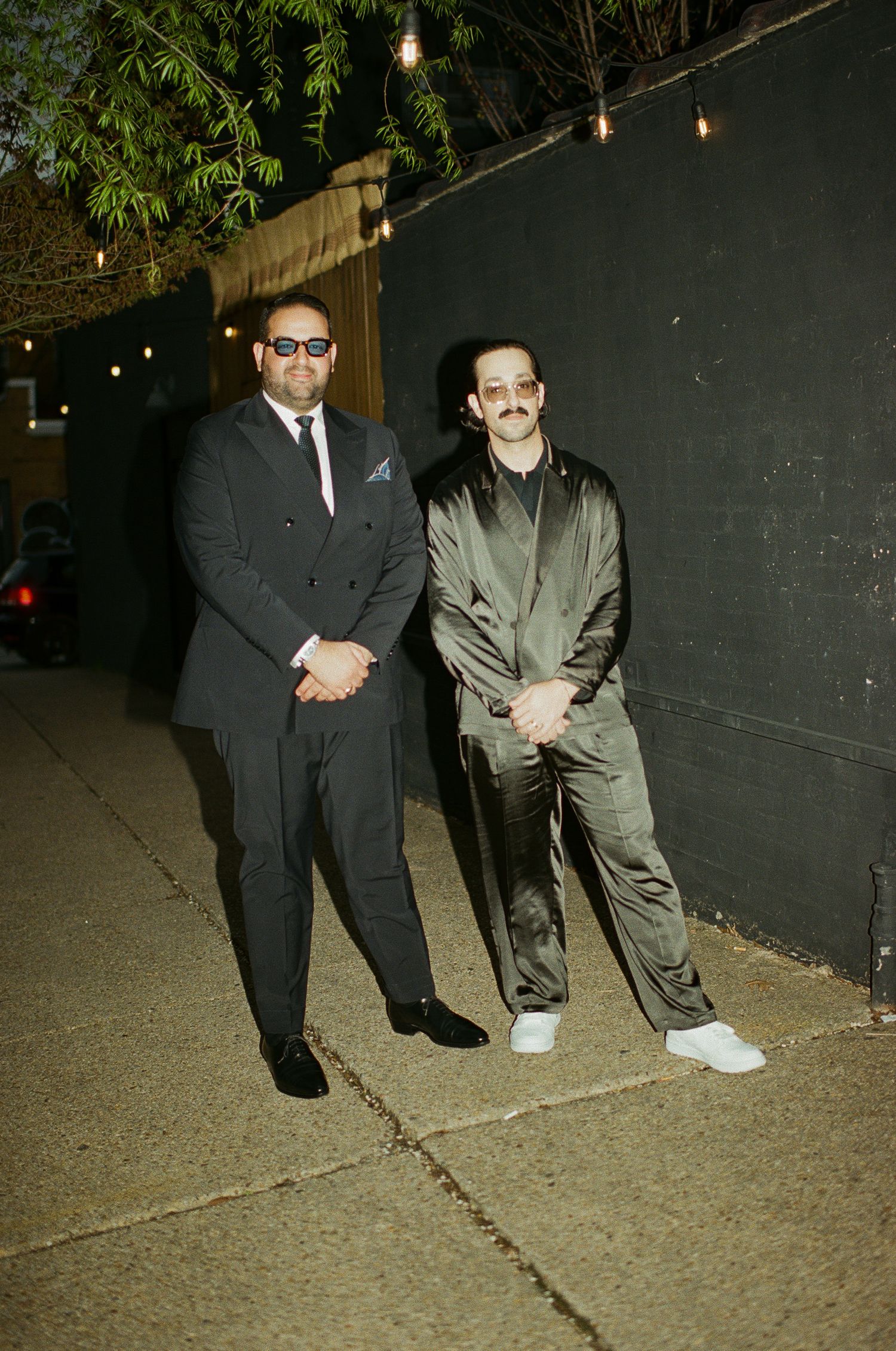 Two people in formal attire standing against a dark wall with string lights overhead at Fadensonnen in Baltimore
