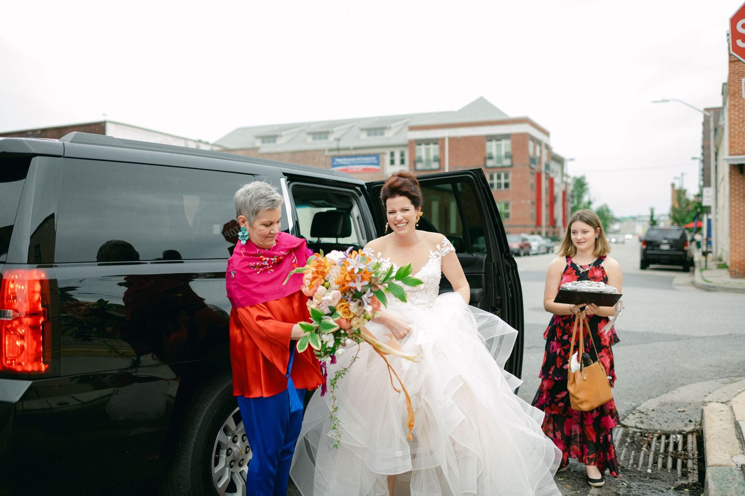Wedding party members assist with transportation outside near a black vehicle.