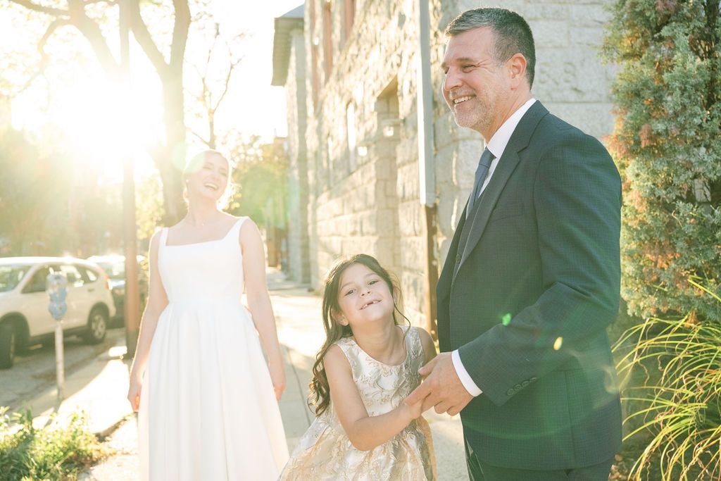 Romantic wedding couple poses in golden sunlight against a brick wall with lush greenery.