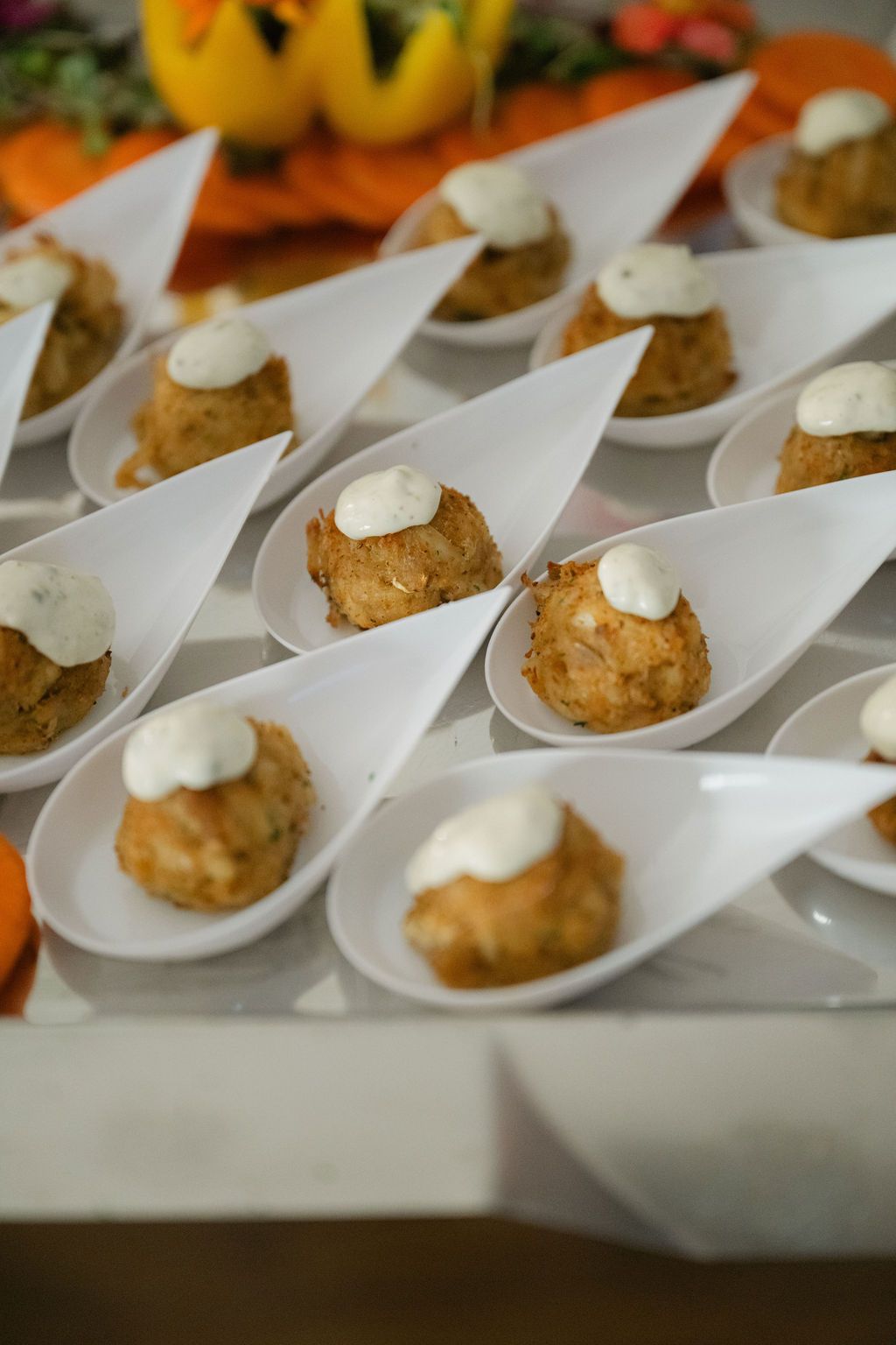 White appetizer plates with crab cakes topped with creamy sauce arranged in neat rows.