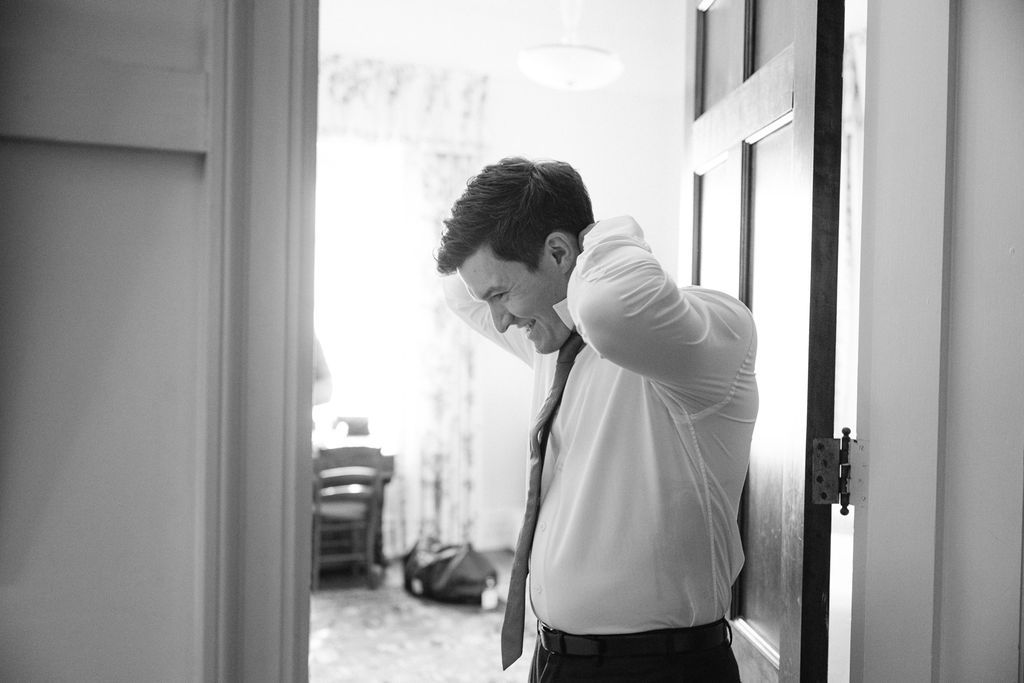 Side profile views of groom preparing in front of window with natural lighting.