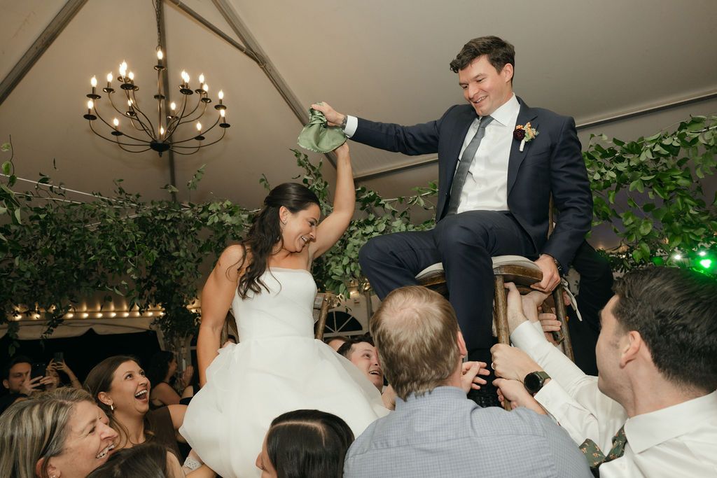 Traditional wedding chair lift celebration during a reception under a tent with chandelier.