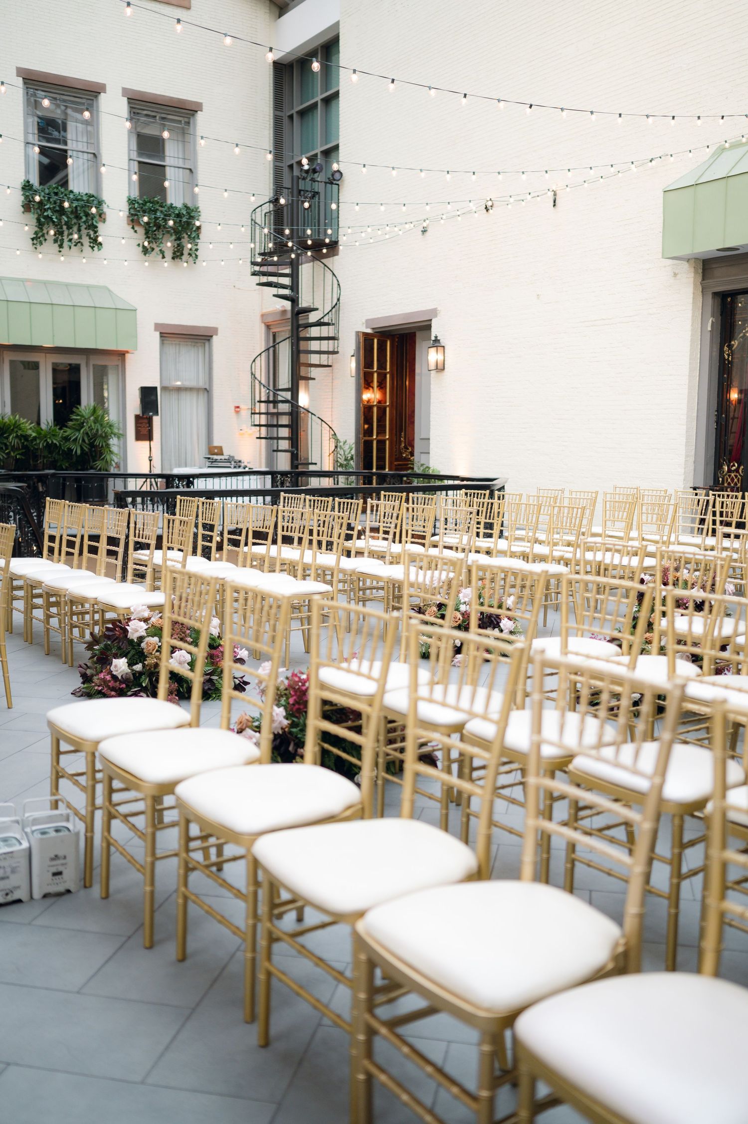 Rows of wooden chairs with white cushions arranged for an outdoor wedding ceremony.