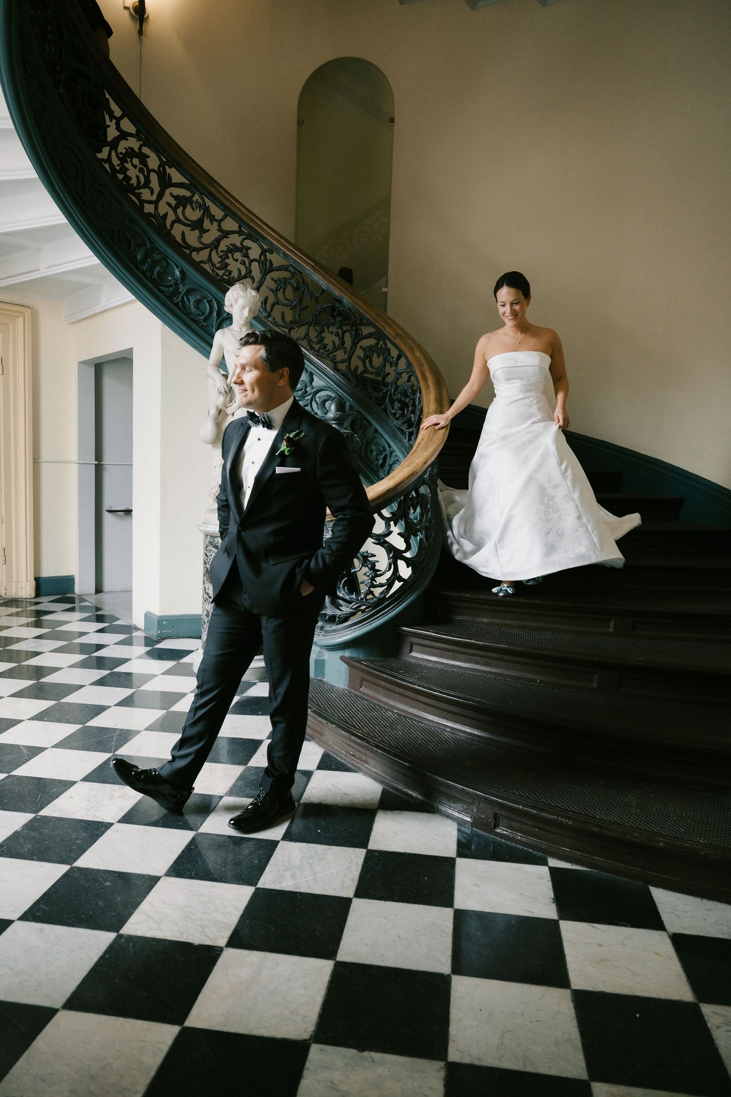 Elegant black and white checkered floor with ornate staircase in historic building.