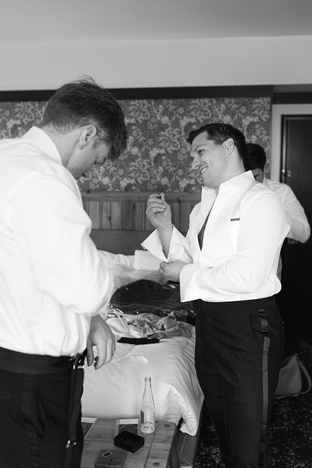 Groomsmen helping each other prepare in formal attire before the wedding ceremony.