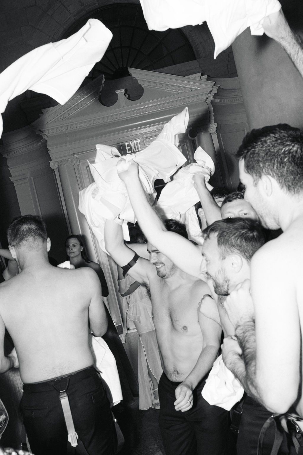 Black and white photo of a crowded party scene with shirtless people dancing and socializing at a nightclub.