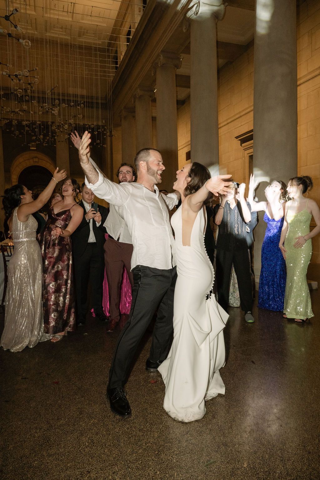 Wedding guests dance and celebrate together on a grand ballroom floor under warm lighting.