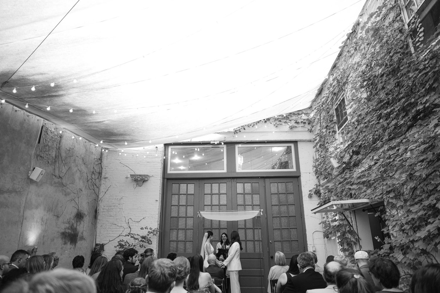 Evening wedding reception with string lights illuminating exposed brick courtyard.