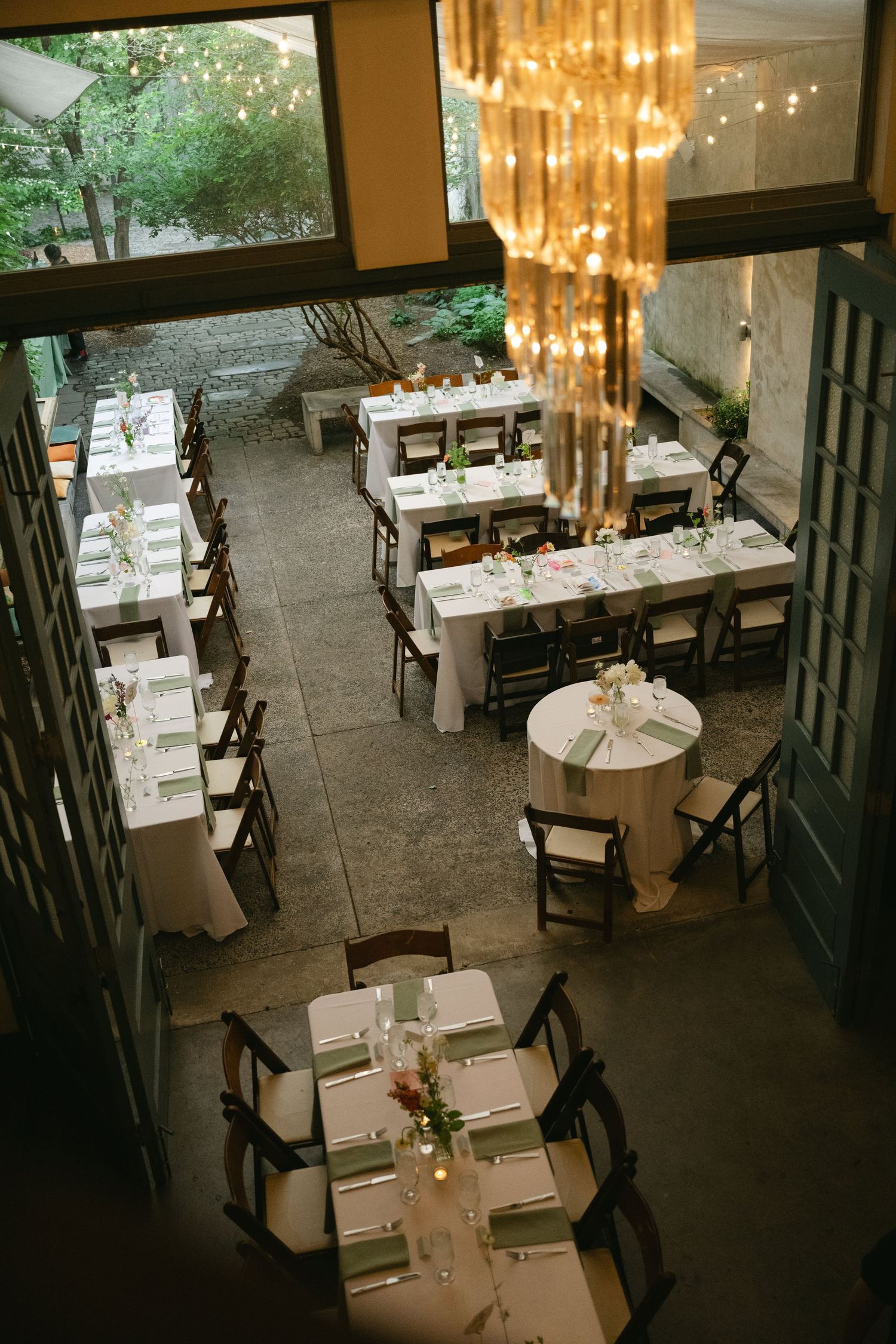 Intimate restaurant interior with chandelier lighting and wooden chairs arranged around white-clothed tables.