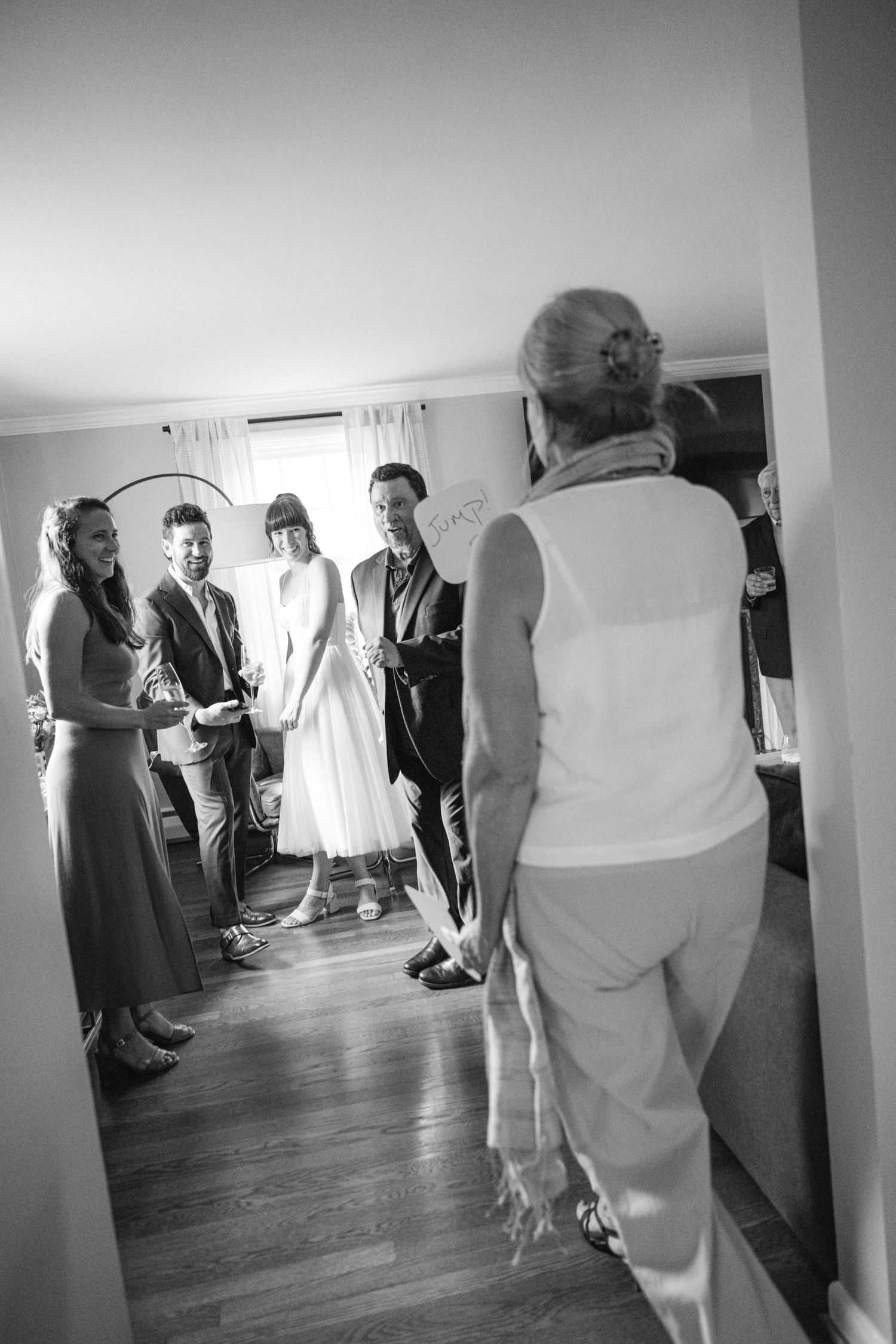 Black and white photo of wedding guests gathering in a room with hardwood floors.