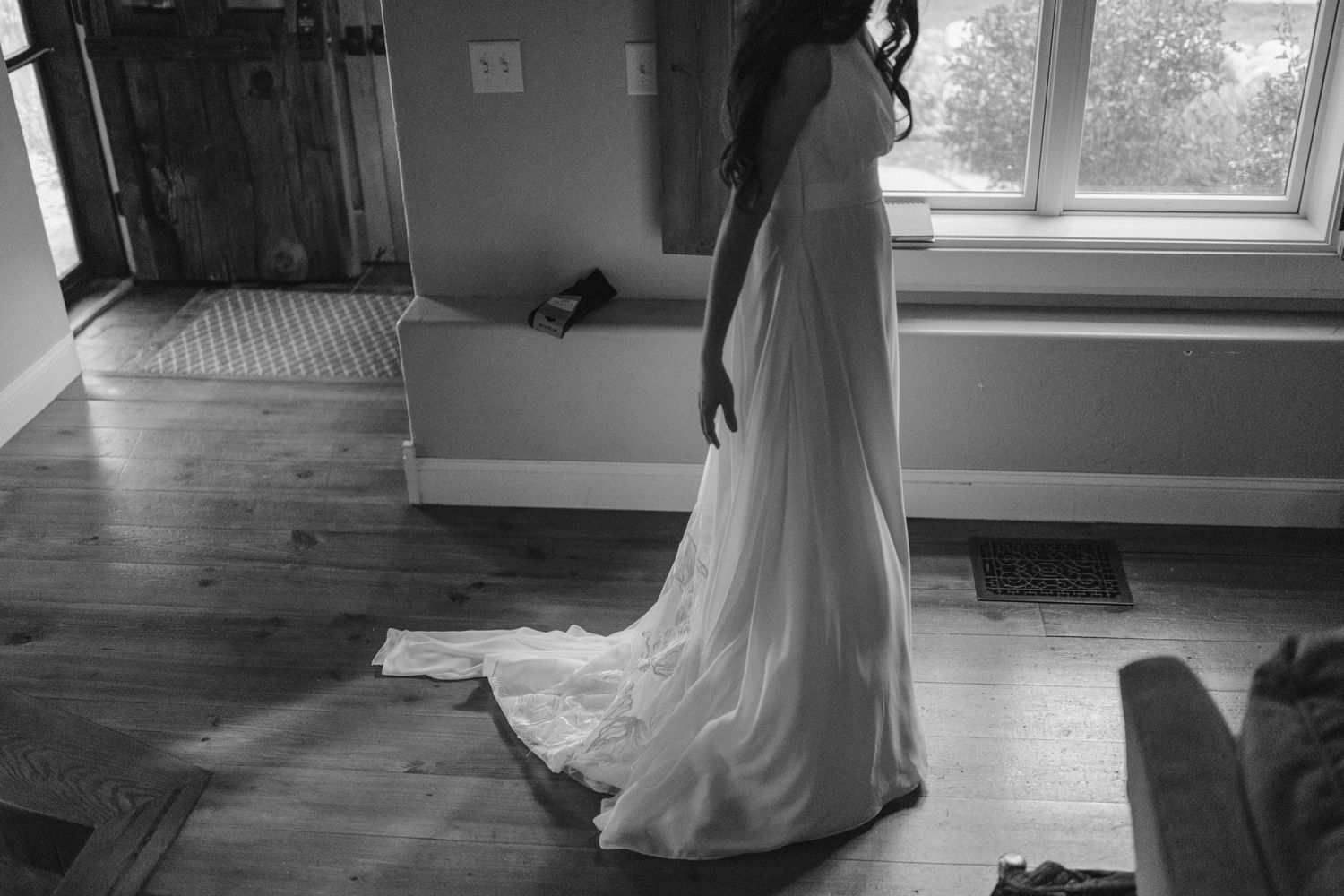 Wedding dress being fitted and adjusted in sunlit room with hardwood floors.