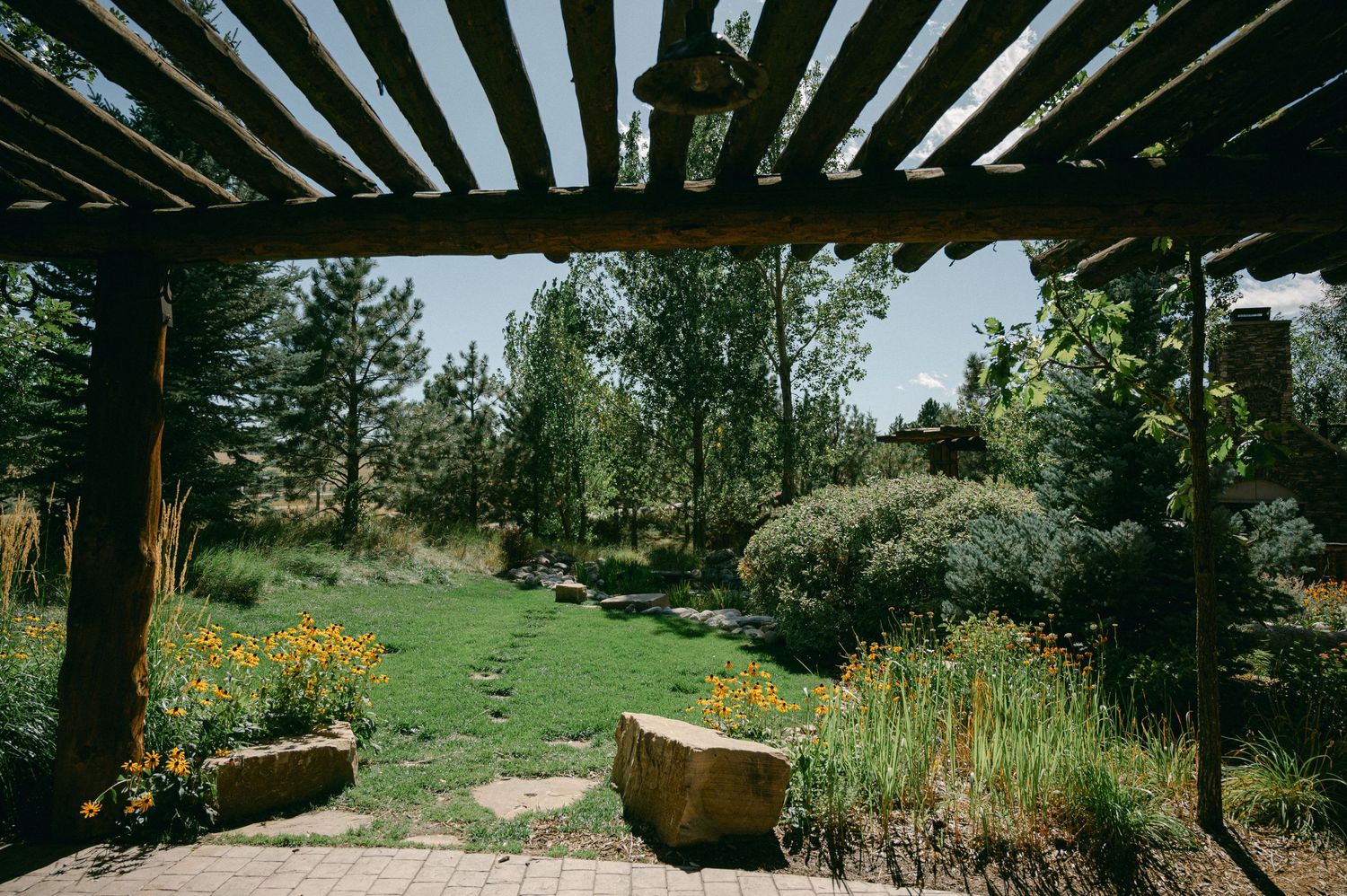 Garden path leading through flowering landscape under wooden pergola.