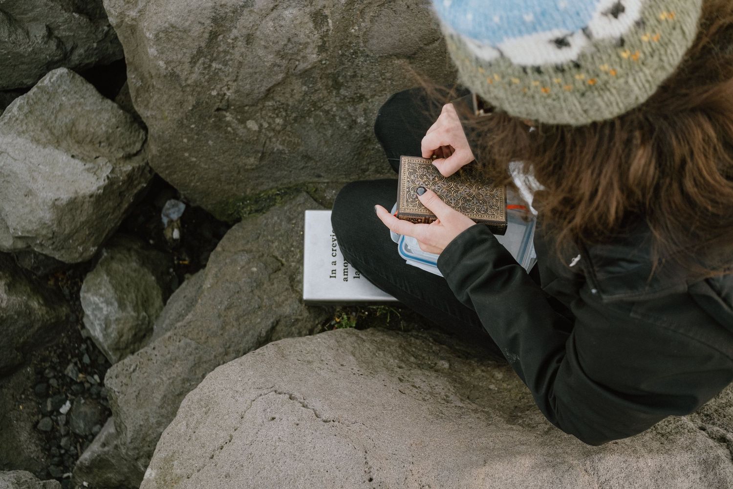 Person writing in a notebook while sitting among coastal rocks.