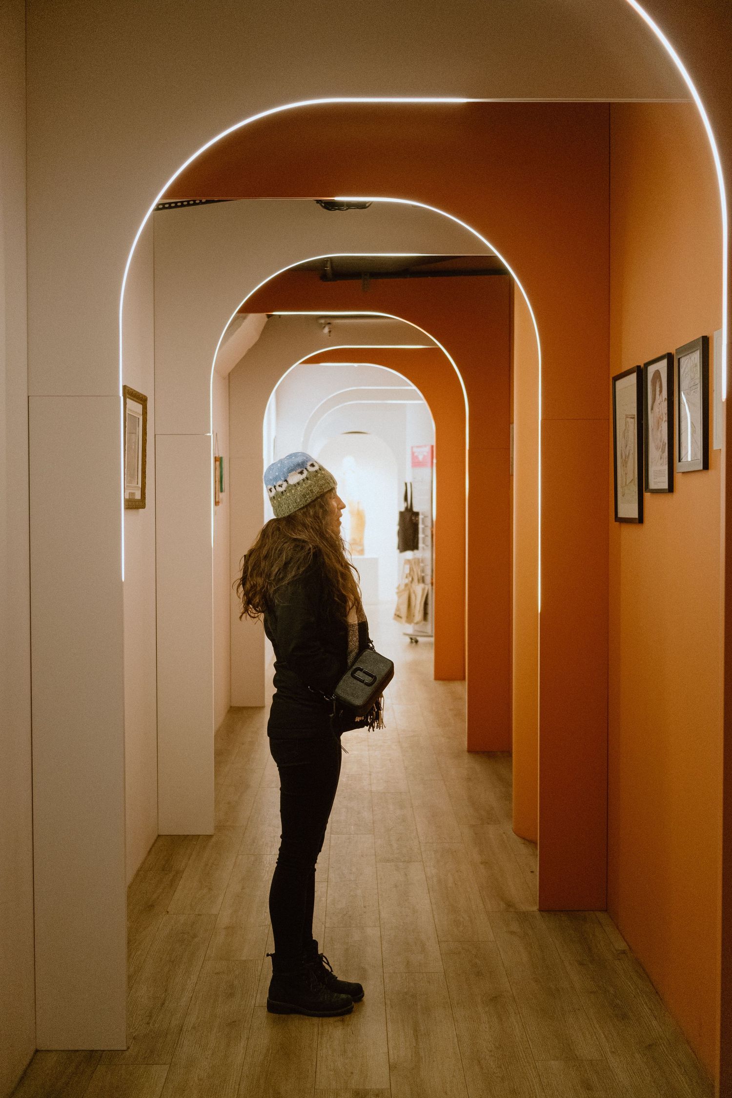 A silhouetted figure stands in an arched hallway with orange walls and framed artwork.