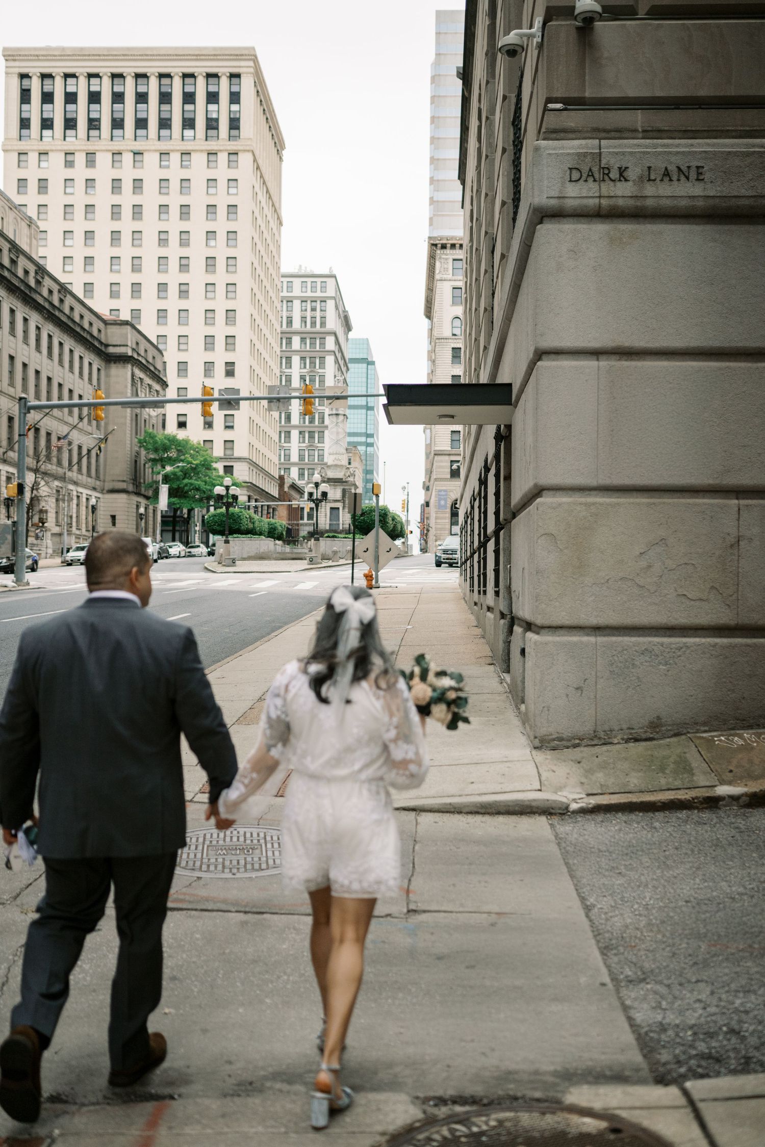 A couple walks down a baltimore city street with historic buildings and architecture in the background.