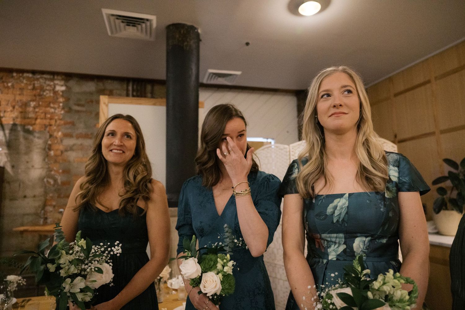 Bridesmaids in navy blue dresses gather together at a wedding celebration with rustic brick wall backdrop.
