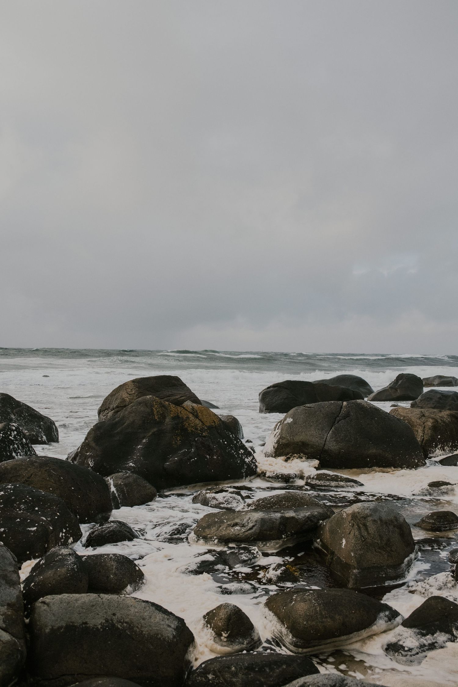 Large boulders scattered along dramatic coastline with waves crashing against rocky shore.