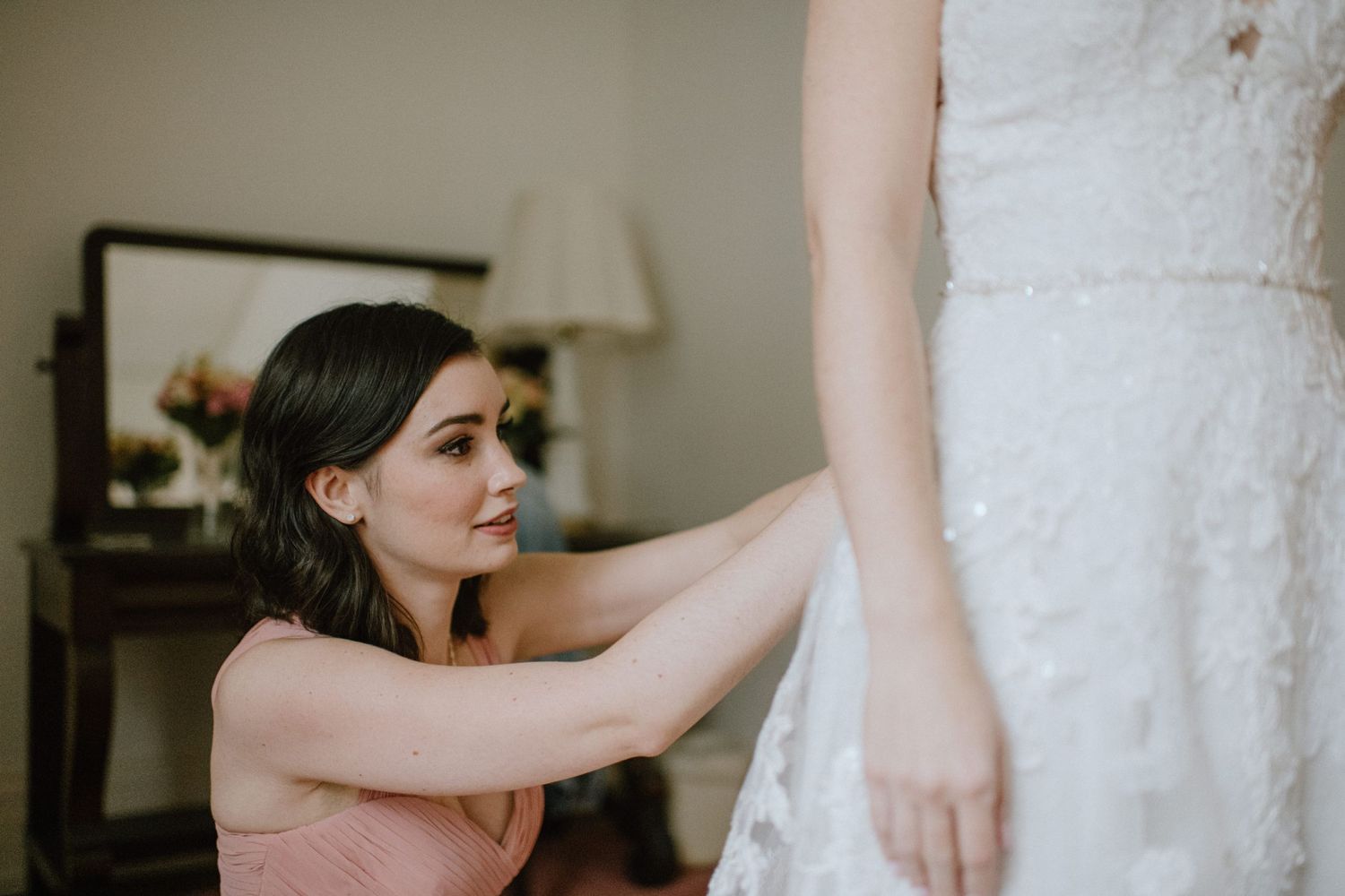 bridesmaid in pink dress helping bride button wedding dress