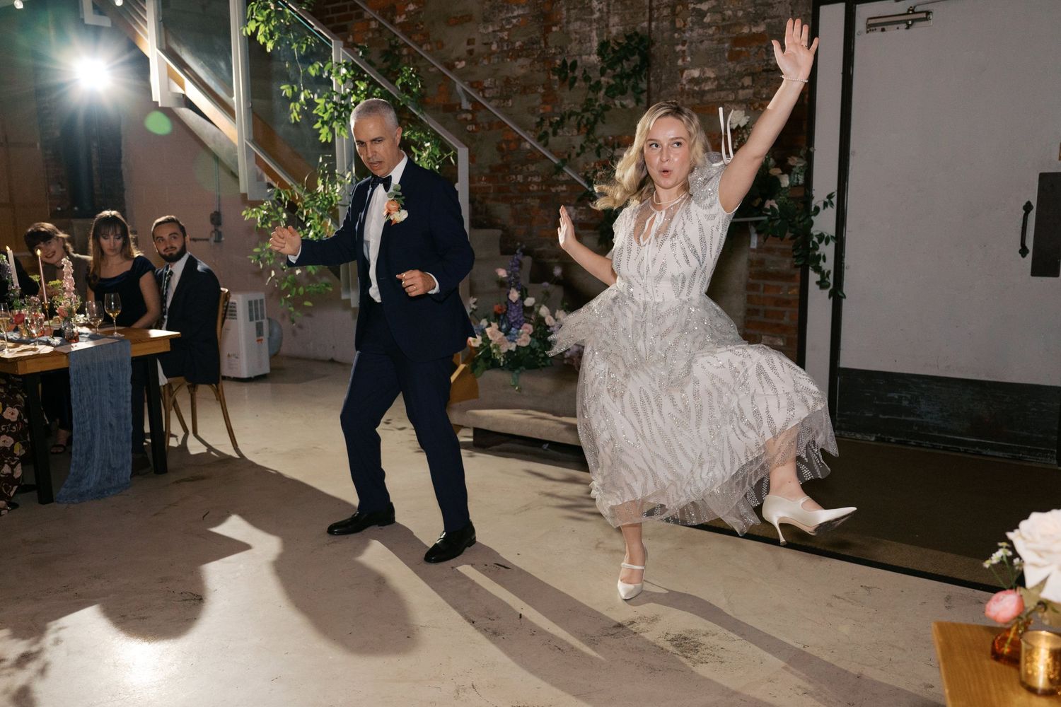 A joyful couple dances energetically at their wedding reception in an industrial-style venue.