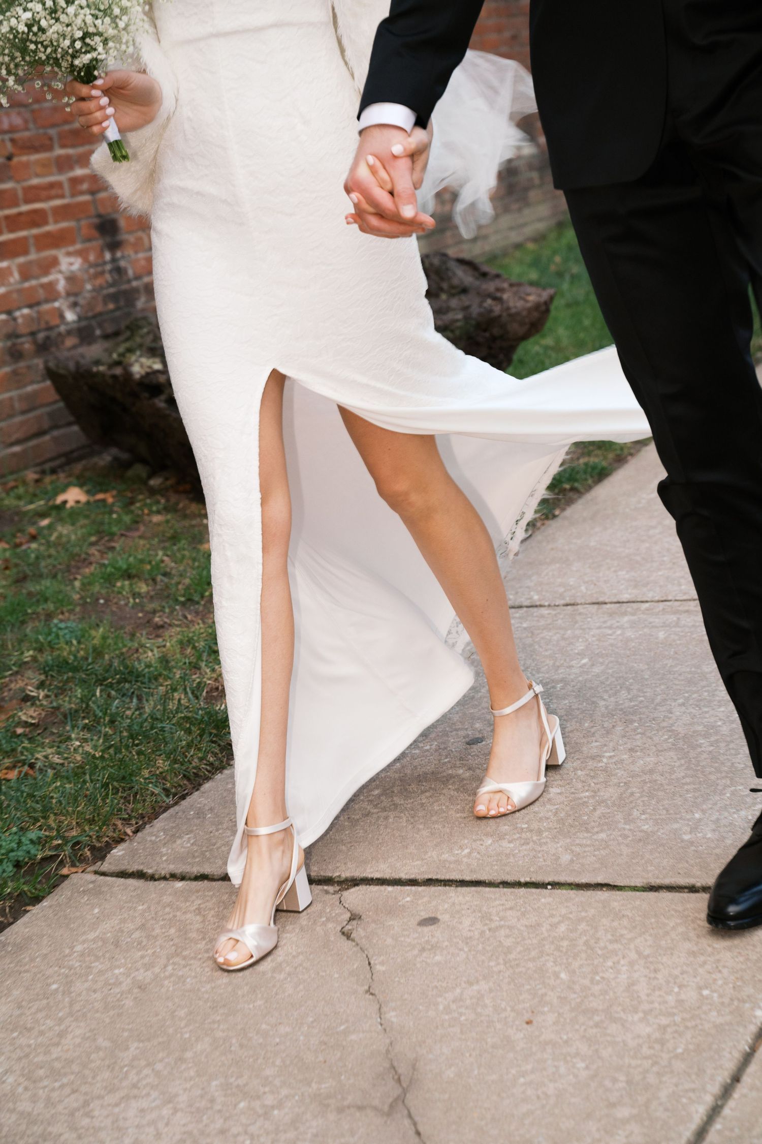 Close-up shot of bride and groom's legs walking together, showing white wedding dress slit and elegant bridal heels.
