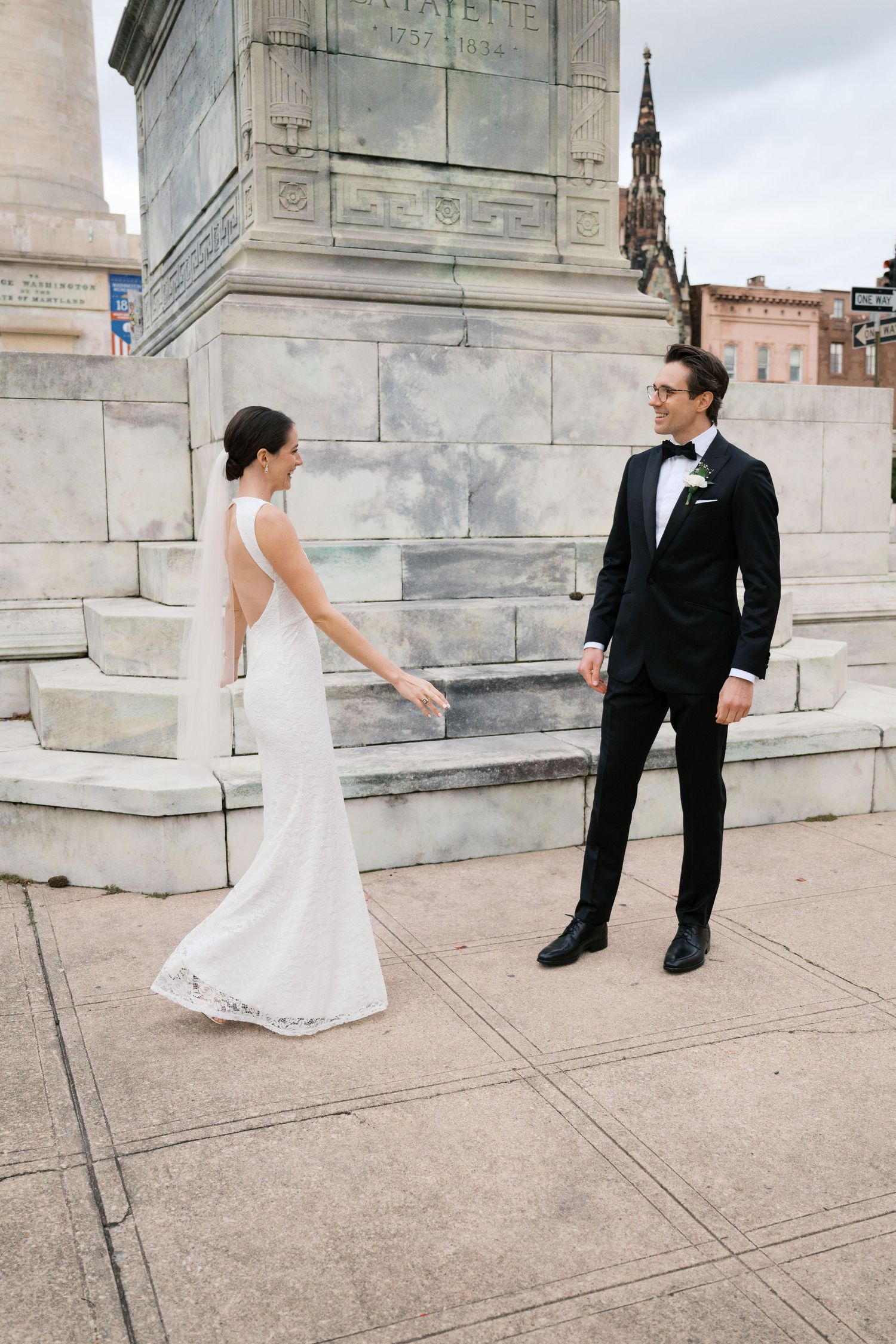 Elegant couple in wedding attire poses on stone steps of historic building.