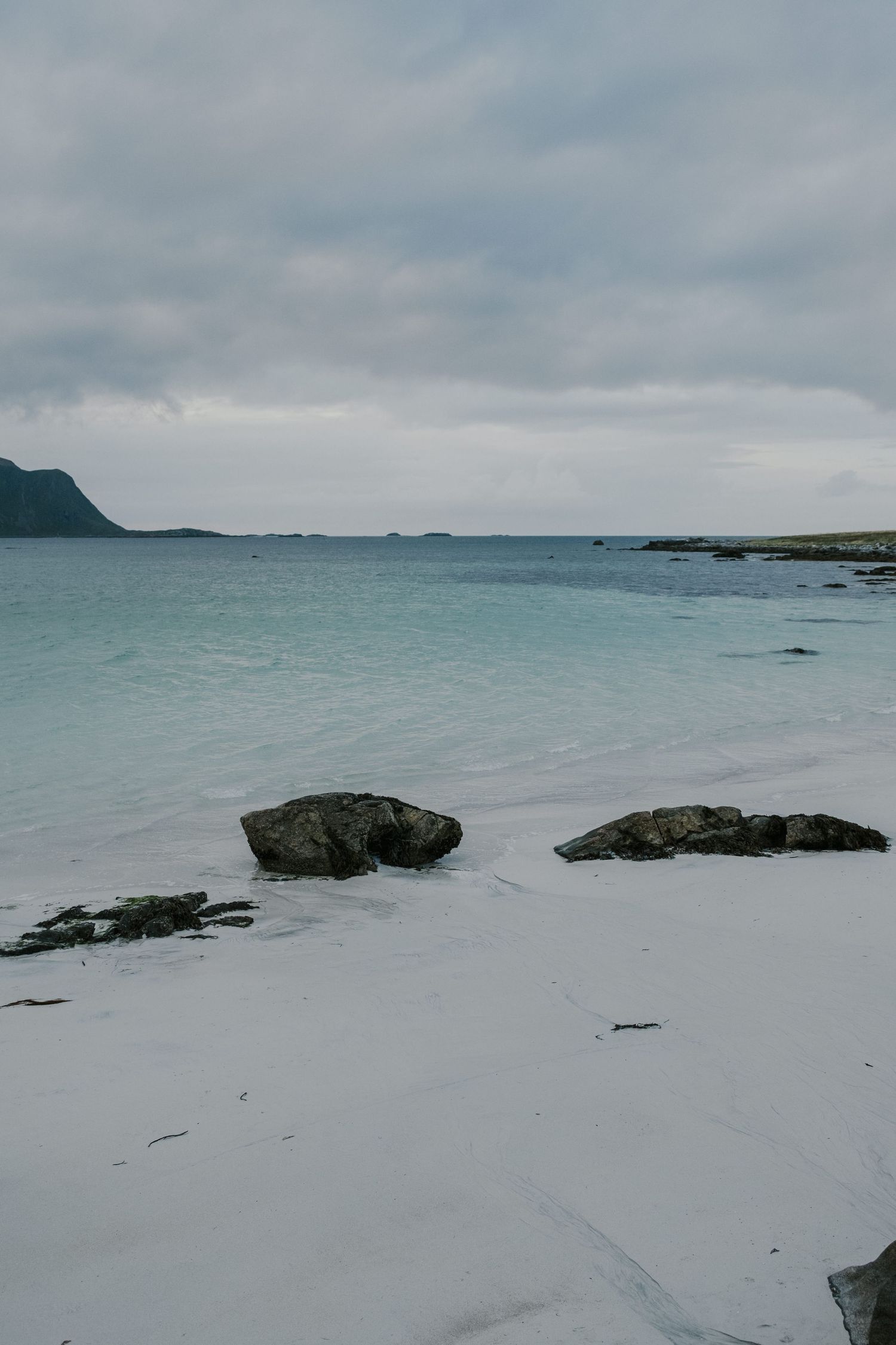 Serene white sandy beach with black rocks and misty mountains in the distance.