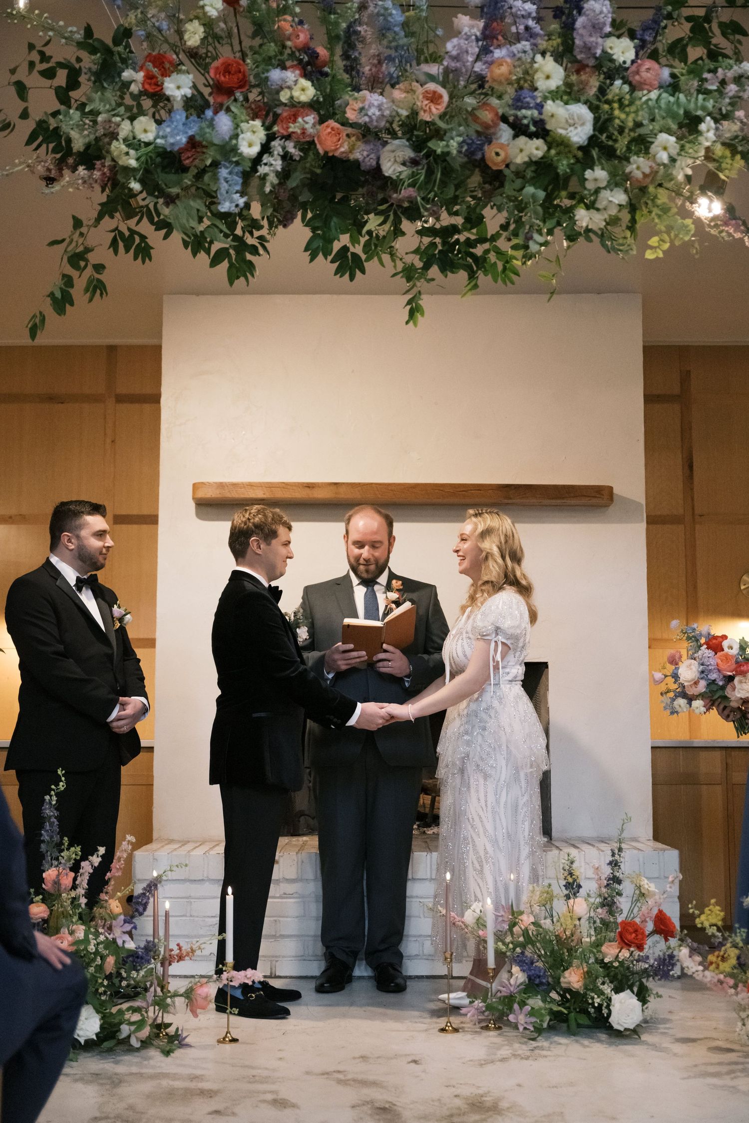Wedding ceremony in progress under beautiful floral installation with rustic wooden accent wall.