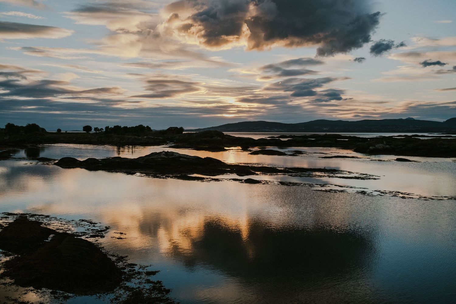 Tranquil coastal scene with sunset clouds reflecting in still water among rocky outcrops.