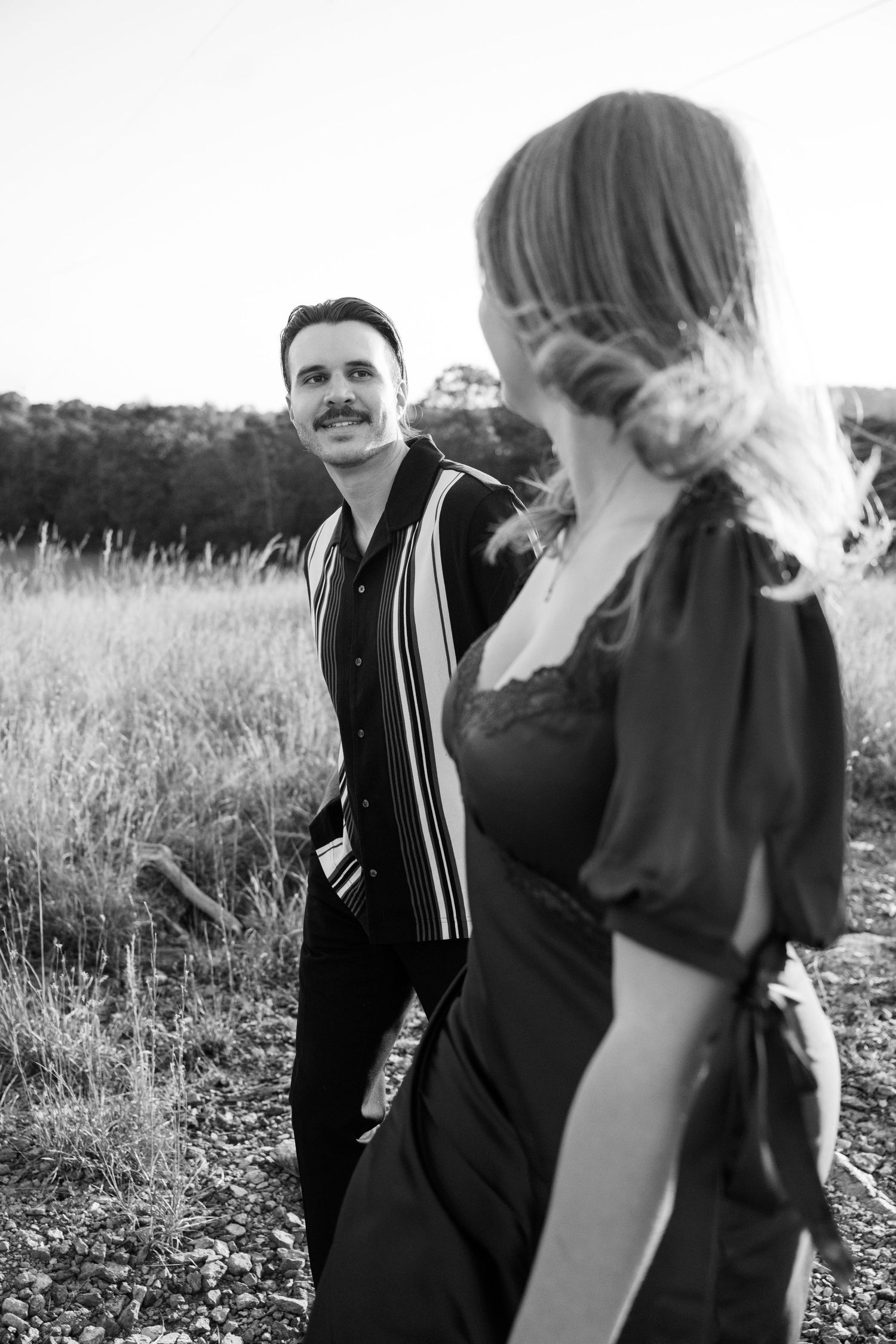 Black and white portrait of a couple in a field at sunset, with natural lighting creating a candid romantic moment.