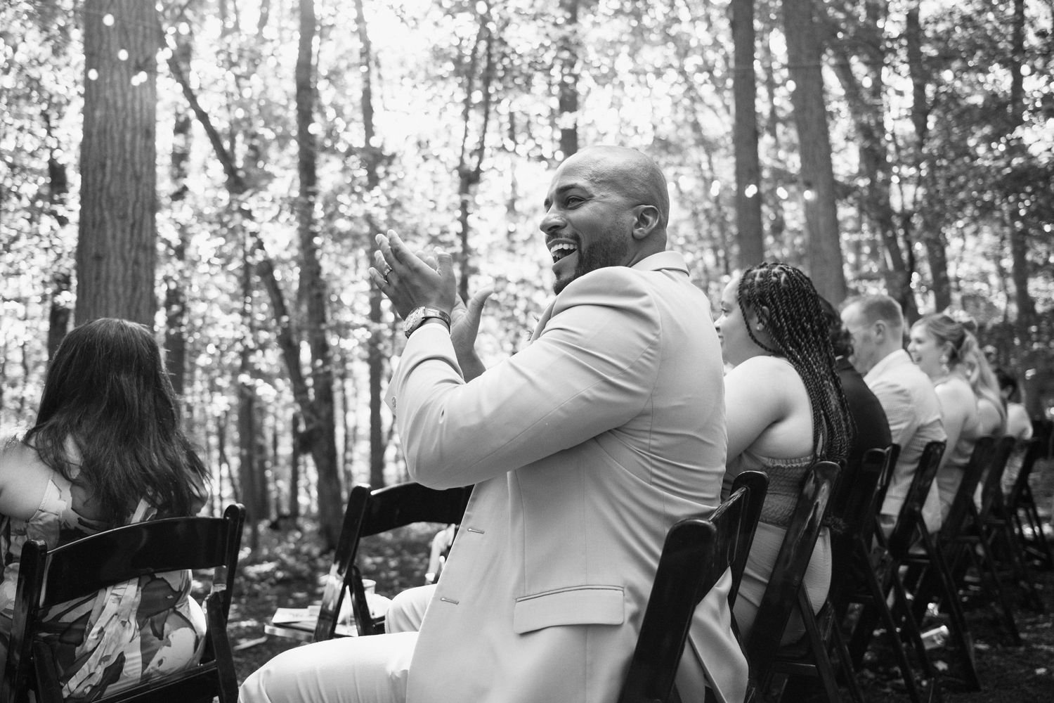 A wedding guest in a light suit reacts emotionally during an outdoor ceremony.
