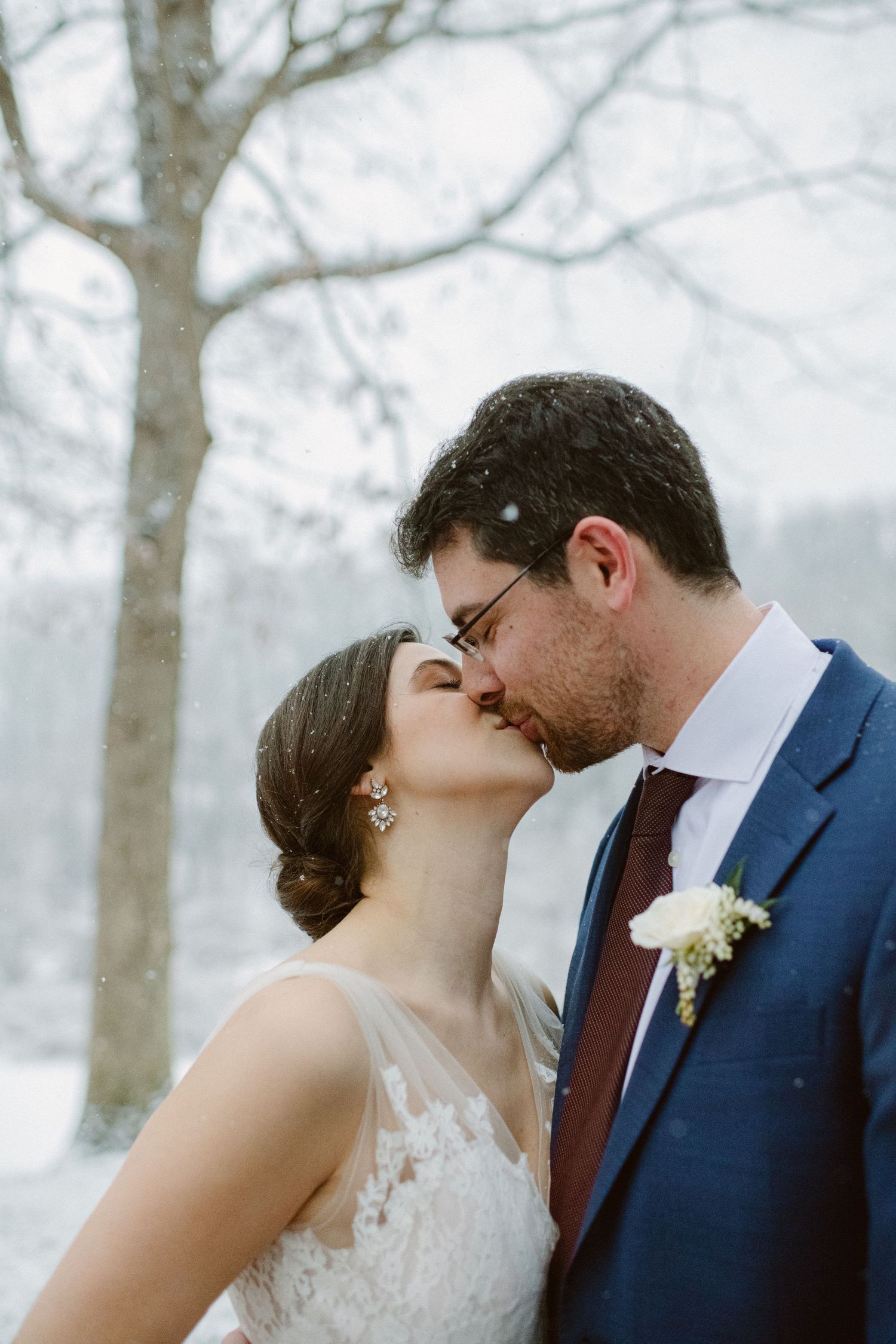 A romantic winter wedding portrait features a couple sharing an intimate kiss against a misty forest backdrop.