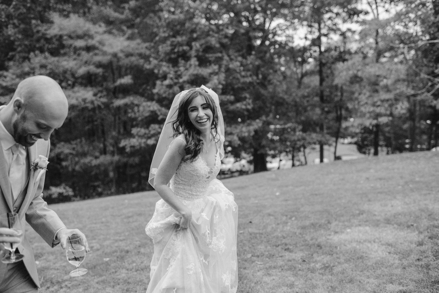 Candid moment captured in black and white as newlyweds share a laugh on grassy hillside.