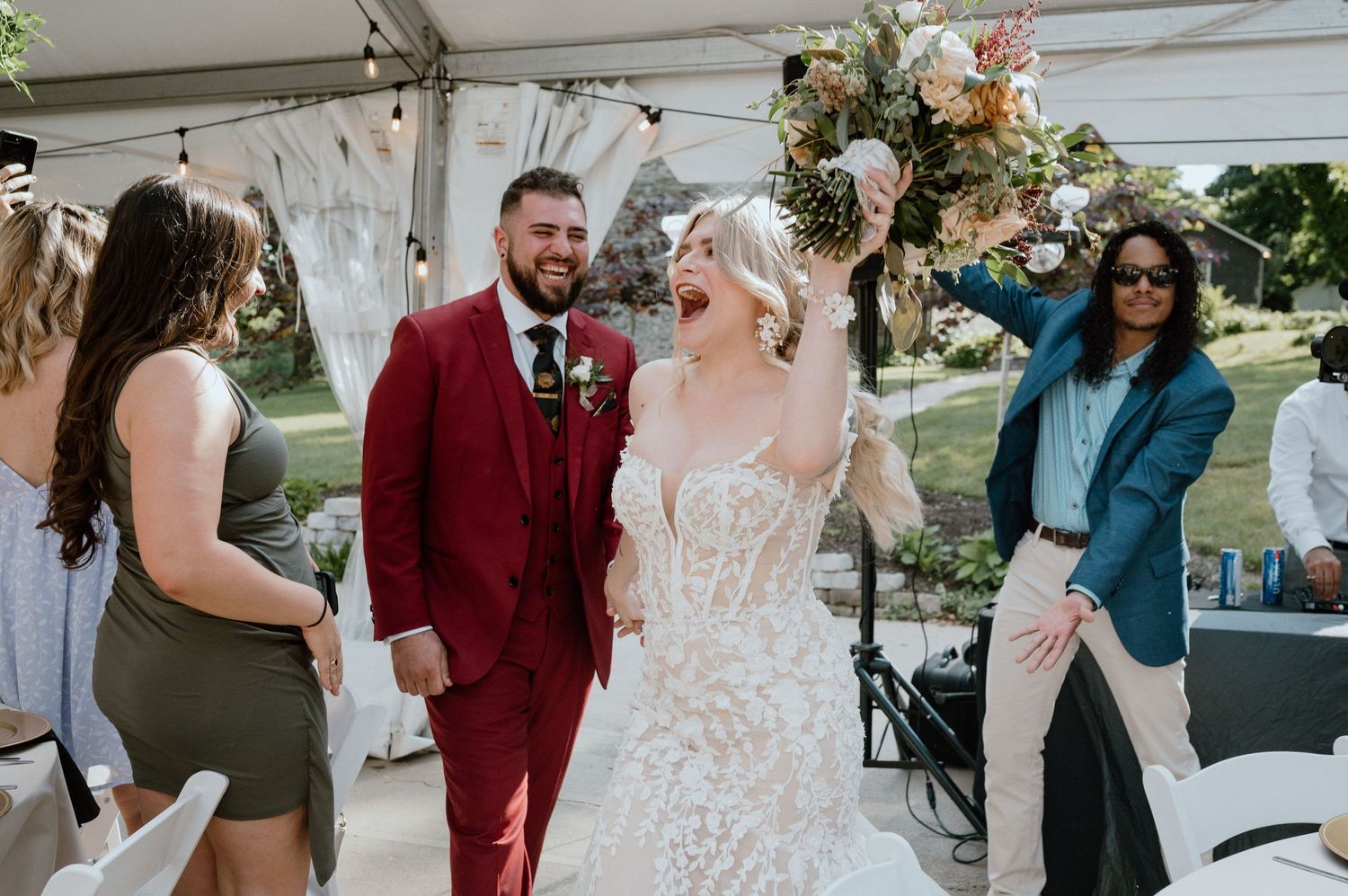 Wedding celebration under a white tent with guests watching.
