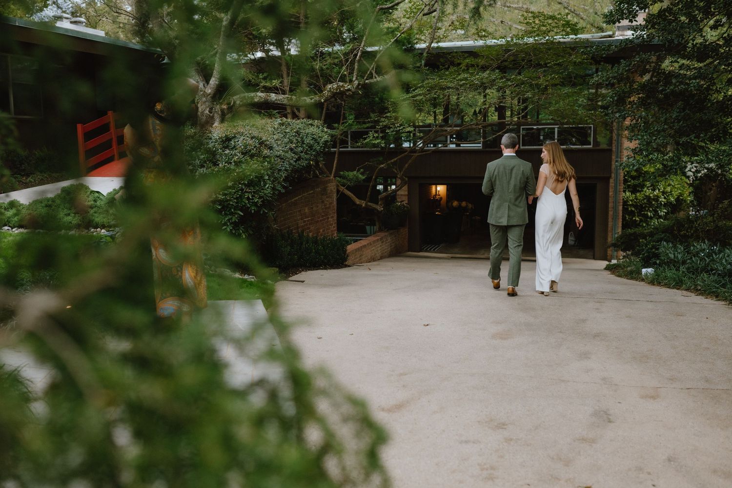 Elegant couple walking down garden path near rustic building entrance.